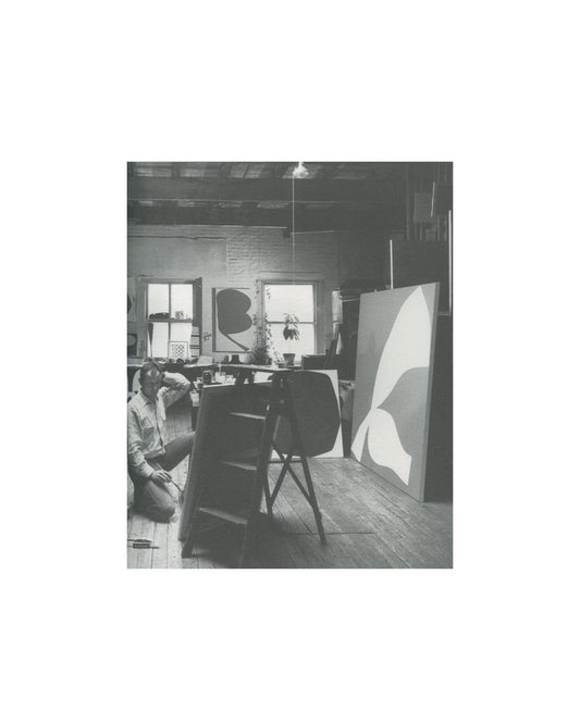Ellsworth Kelly — A Salute to Ellsworth Kelly, 1999 — interior plate. Black and white photograph of Ellsworth Kelly seated on the floor of his studio, working at low level. Two large canvases with biomorphic curved forms visible in background. Worktable and studio equipment in mid-ground.
