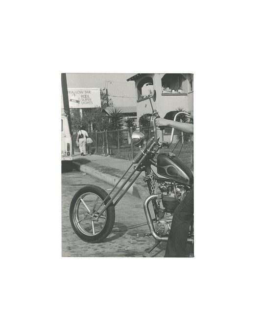 Reverse of 2011 Janette Beckman El Hoyo Maravilla, Dashwood Books. Back cover showing near-blank white wrapper with small inset black-and-white photograph of a chopper motorcycle parked on a suburban street with a Kool cigarettes billboard visible behind.