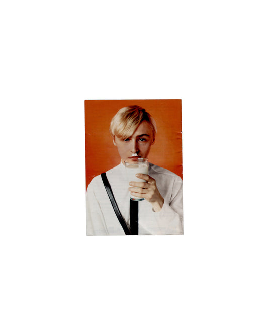 Back cover General Idea, Haute Culture: Une rétrospective, 1969–1994, Musée d'Art moderne de la Ville de Paris, 2011. Booklet back cover: colour photograph of a single figure against vivid orange-red ground — short blonde hair, white top, black diagonal strap, holding a glass of milk to lips; direct gaze. Handling creases, small mark lower cover.