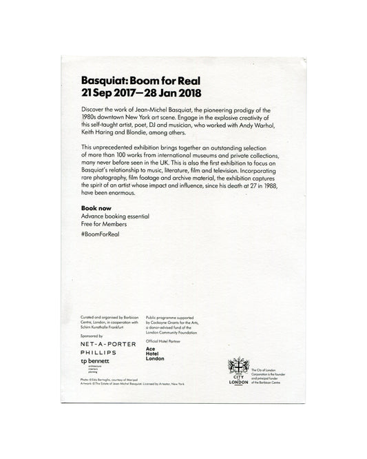 Promotional card verso, Jean-Michel Basquiat: Boom for Real, Barbican Art Gallery, London, 2017. White ground. Bold black sans-serif header — 'Basquiat: Boom for Real / 21 Sep 2017—28 Jan 2018'. Two paragraphs of exhibition text describing Basquiat as 'pioneering prodigy of the 1980s downtown New York art scene' and noting 100+ works from international collections. Bold text: 'Book now / Advance booking essential / Free for Members / #BoomForReal'. Lower section: institutional credits — curated by Barbican