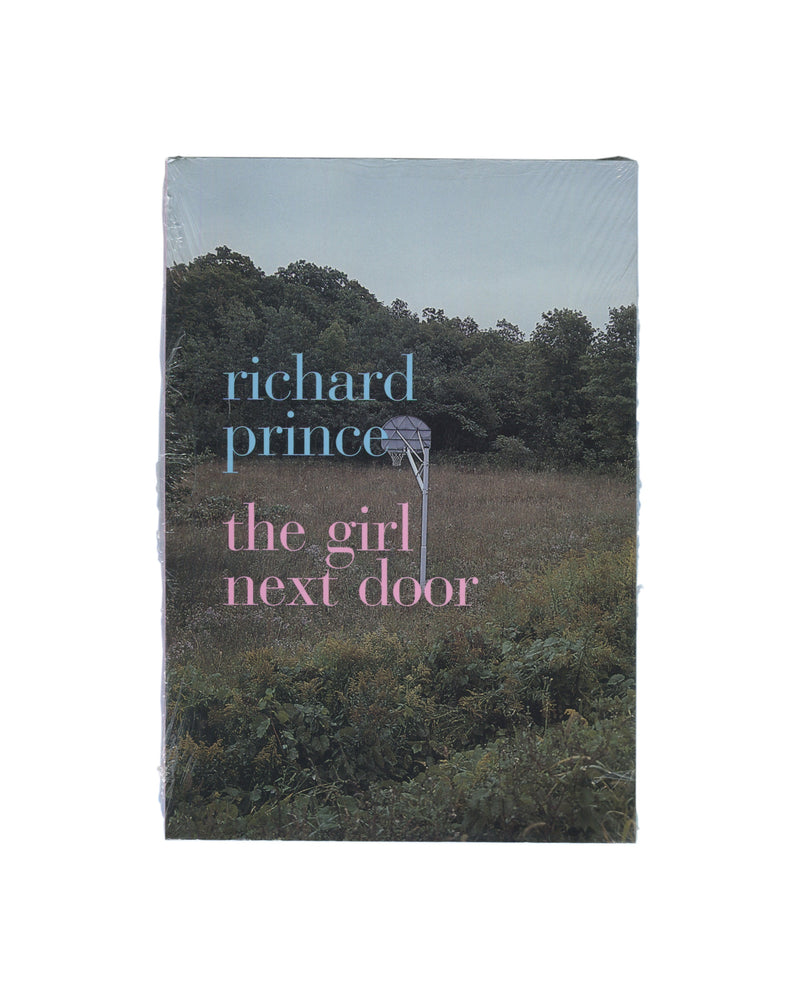 Front cover of Richard Prince’s The Girl Next Door, still sealed in original shrinkwrap, showing a rural overgrown landscape with a basketball hoop and blue and pink title typography.