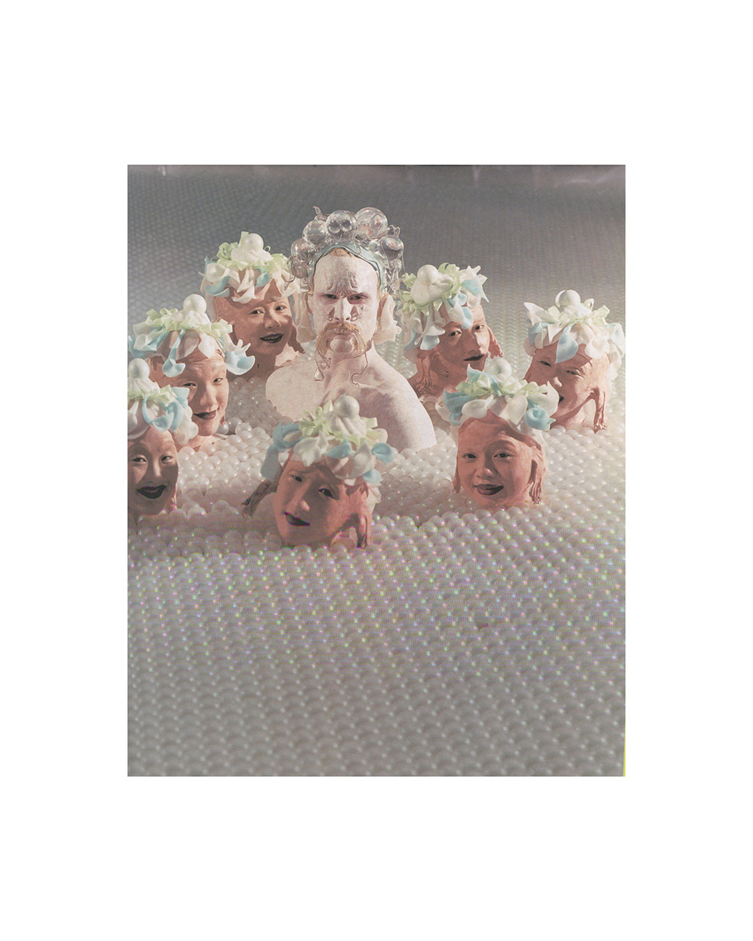 Interior page from 2007 Matthew Barney Supercontemporary, Electa. Showing a production photograph of multiple figures with elaborate floral and bubble headdresses submerged in a field of white pearled material, Barney at centre.