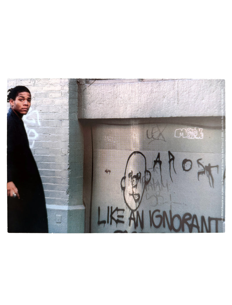 Basquiat standing next to a wall with graffiti and text