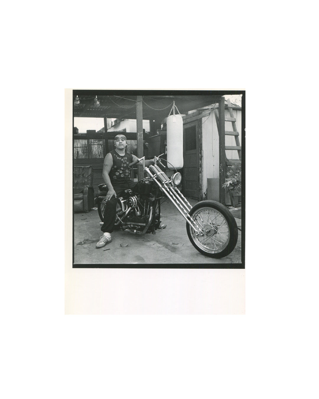 (portrait — man, motorcycle): Interior spread showing black-bordered portrait of a man in a sleeveless vest and headband seated on a chopper motorcycle in a backyard with a punching bag hanging behind him.