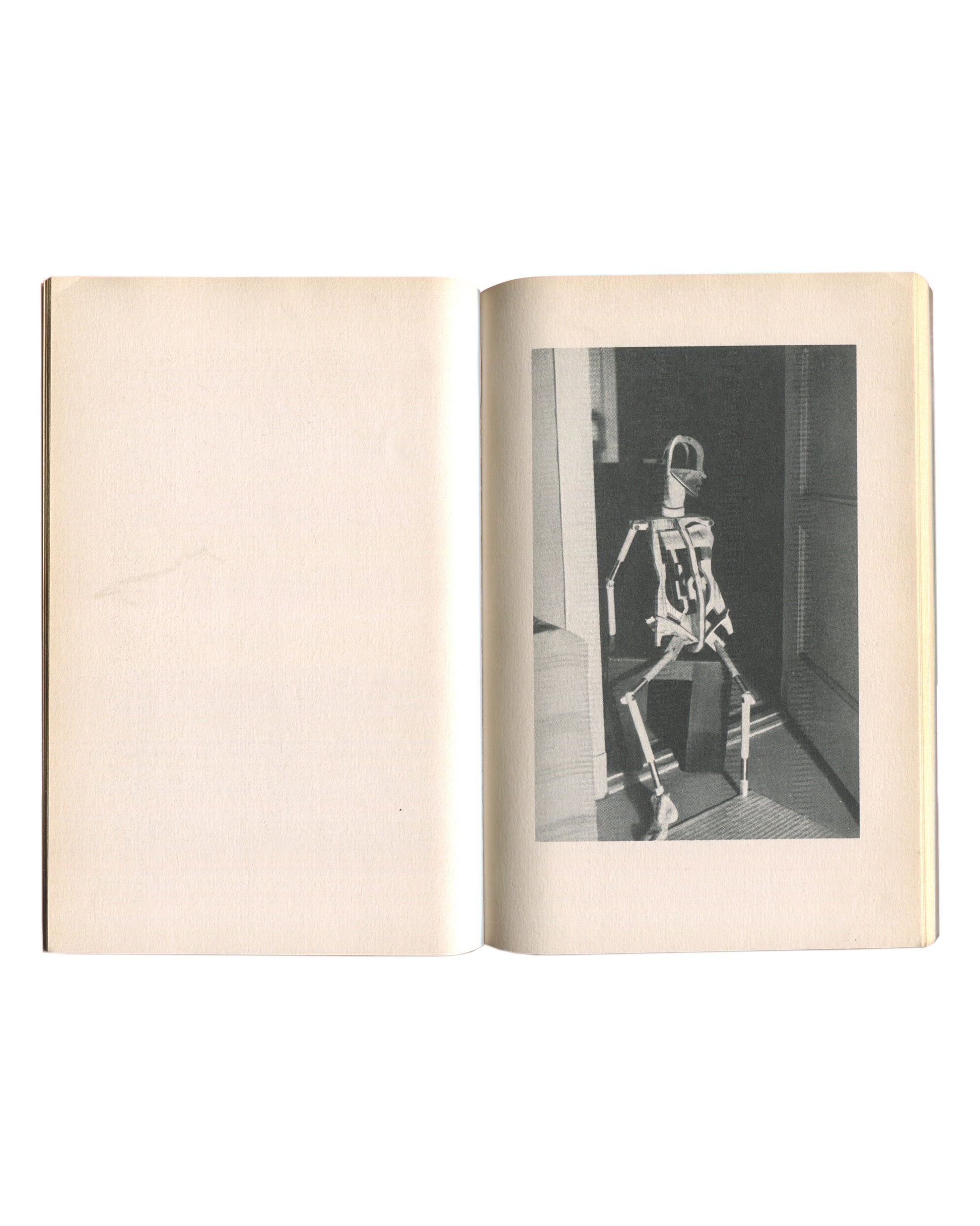 Interior spread of 1976 Hans Bellmer Die Puppe — left page with black-and-white photograph of an articulated skeletal doll figure standing upright in a doorway; right page blank
