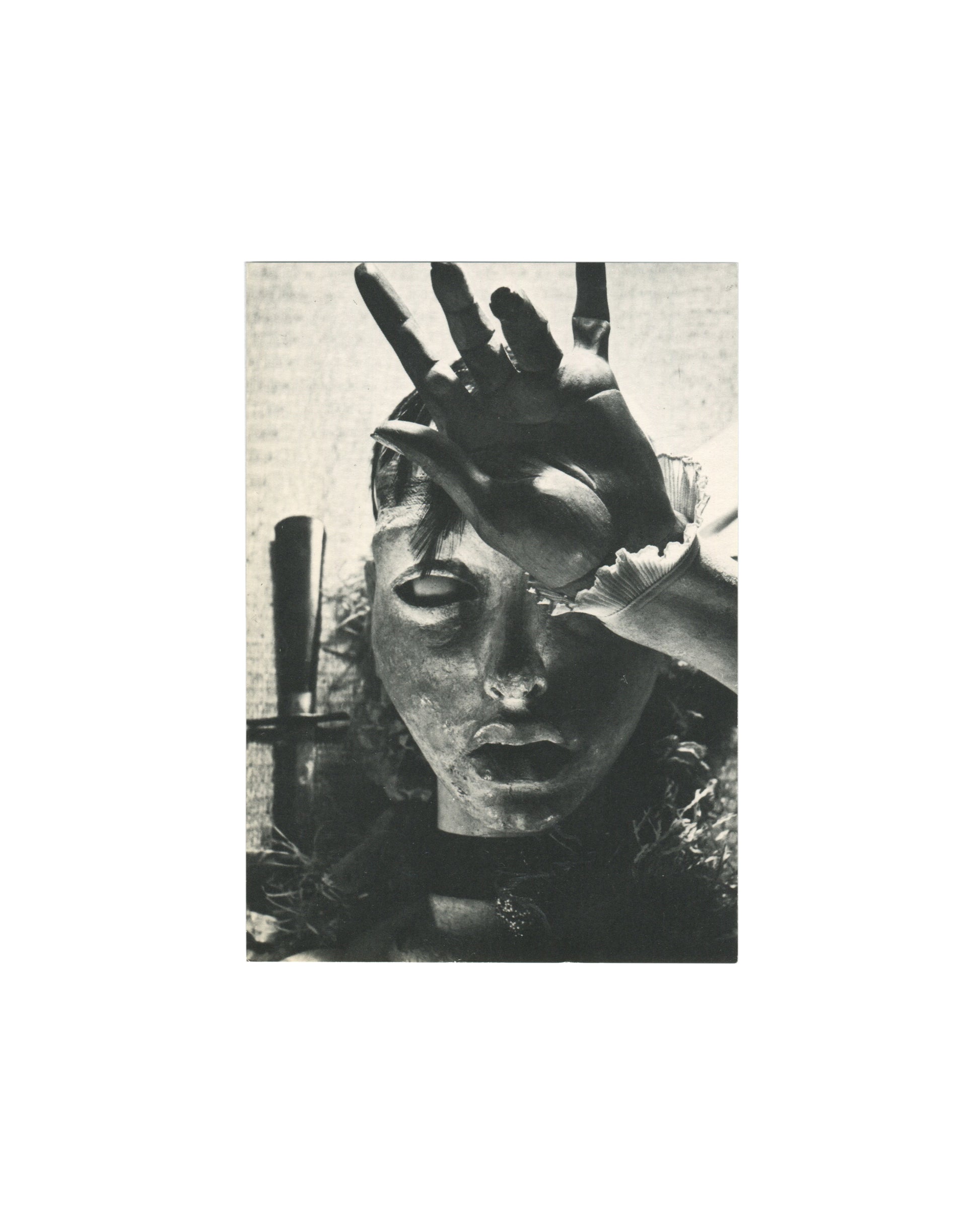 Original 1983 Hans Bellmer exhibition invitation, Galerie François Petit, Paris — recto reproducing a black-and-white photograph of a doll's face partially obscured by a large hand pressing across the eyes and forehead, a cross-shaped object visible at left margin; from the series of doll photographs for which Bellmer is known.