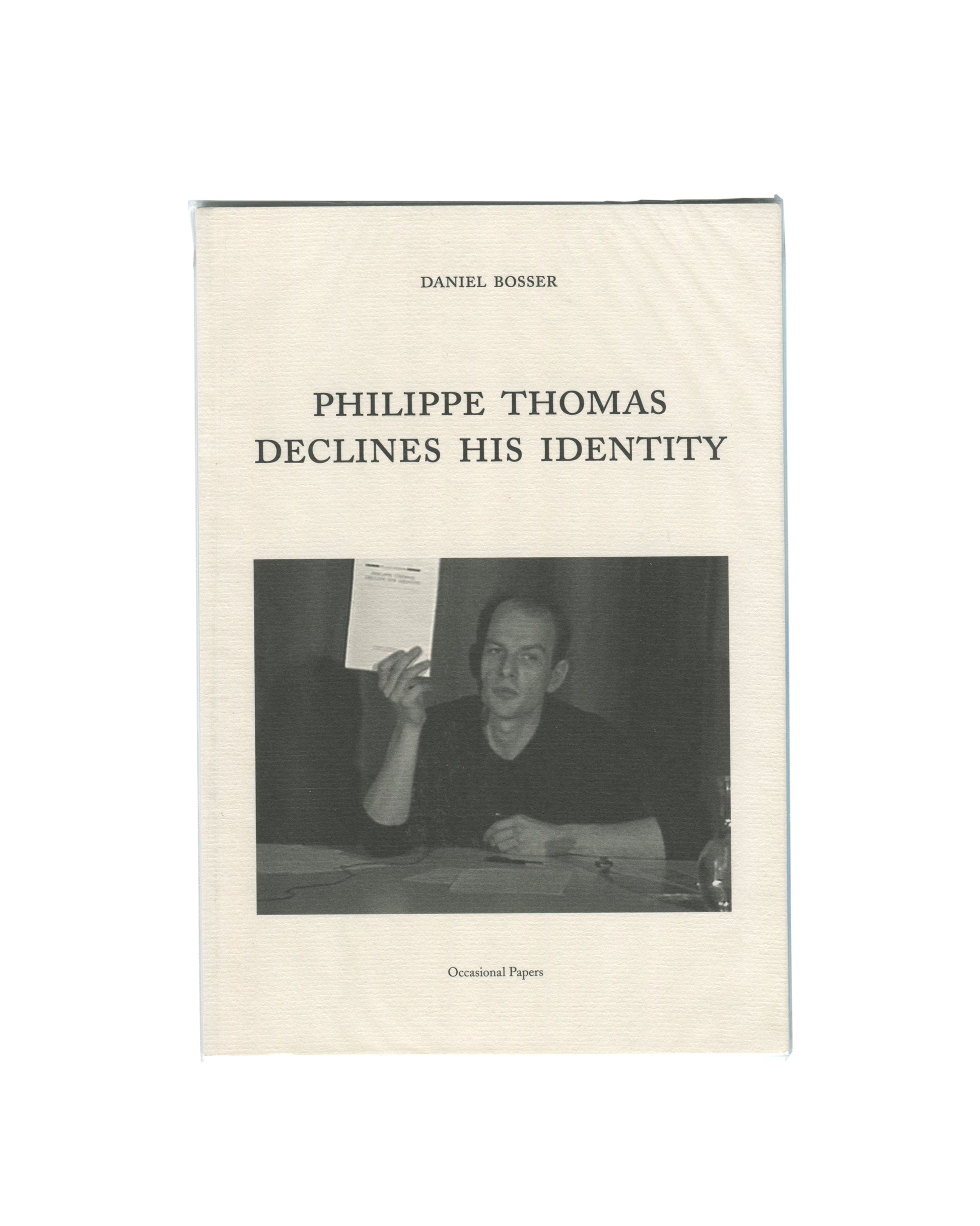 Original 2015 Daniel Bosser, Philippe Thomas Declines His Identity, Occasional Papers, London. Cream textured softcover with 'DANIEL BOSSER' in small spaced serif capitals at top, 'PHILIPPE THOMAS / DECLINES HIS IDENTITY' in larger spaced serif type at centre, and a black-and-white photograph below showing Philippe Thomas seated at a table, holding up a document, wearing a black top, expression direct and slightly confrontational. 'Occasional Papers' in italic type at foot.