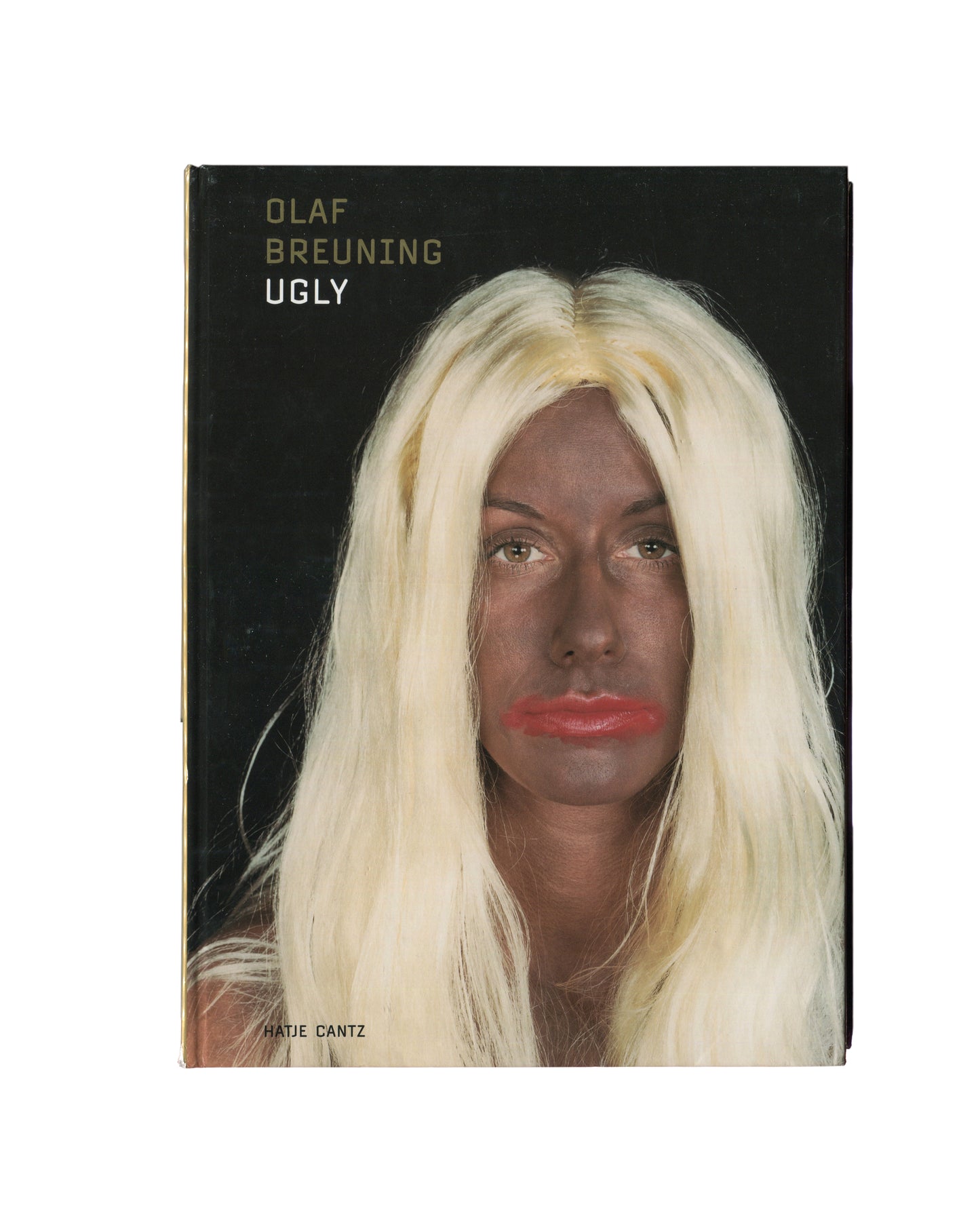 Original 2001 Olaf Breuning Ugly, Hatje Cantz, Ostfildern-Ruit — hardcover front showing full-bleed colour photograph of a young woman in round sunglasses, white crop top, and shoulder holster, holding a pistol raised to shoulder height and a power drill at hip, standing in a narrow wooden doorway, red lipstick, direct gaze