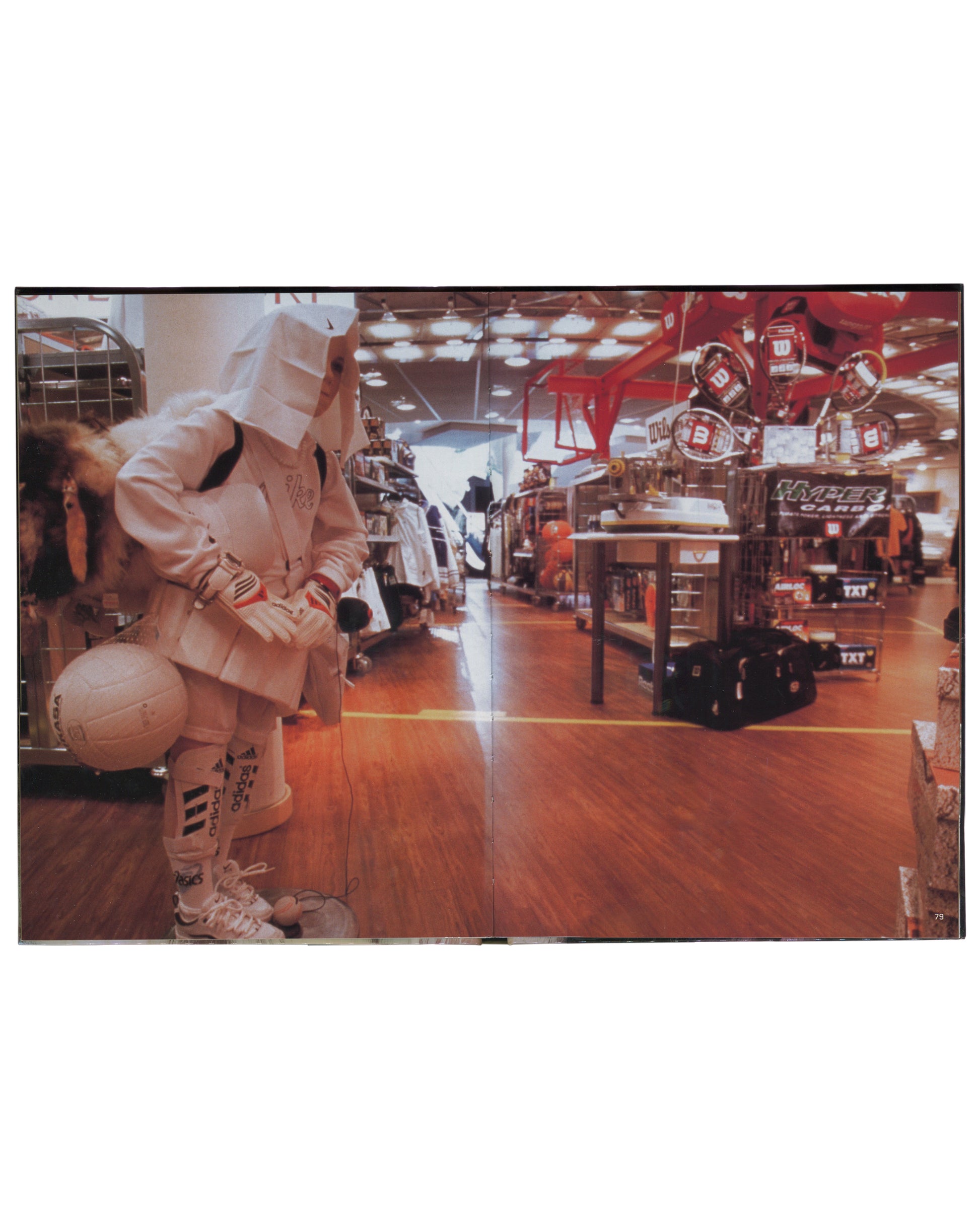 Interior spread of 2001 Olaf Breuning Ugly — full-bleed colour photograph of a figure in a white paper-bag mask, white Adidas tracksuit, and white trainers crouching in a large sports retail store, holding a football, Wilson tennis racket displays and Hyper Carbon signage visible in background