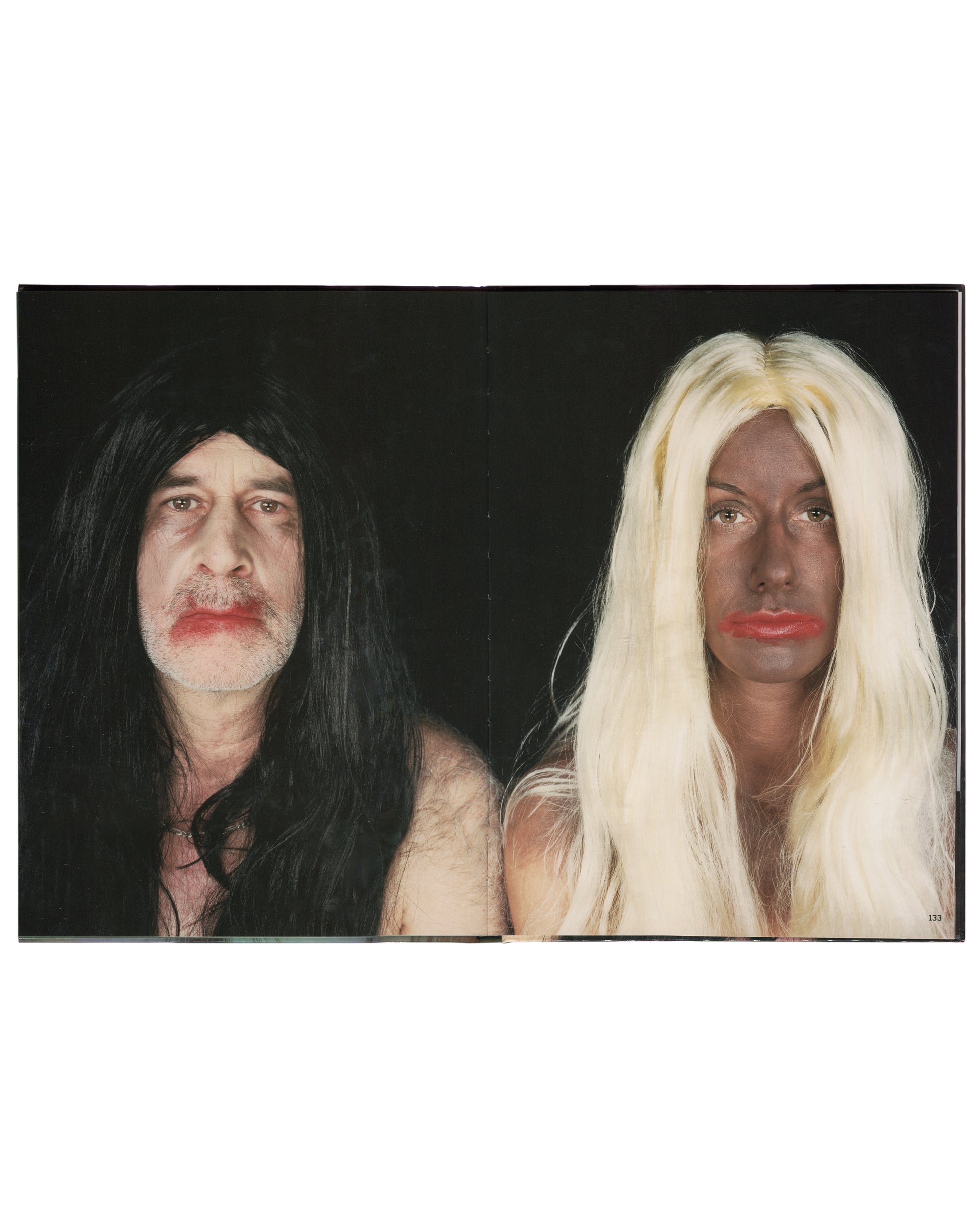 Interior spread of 2001 Olaf Breuning Ugly — full-bleed colour photograph of two figures against a black background: left, a man with long black hair, moustache, and red lipstick; right, a figure with dark skin makeup, long blonde wig, and red lipstick, both bare-shouldered, facing camera