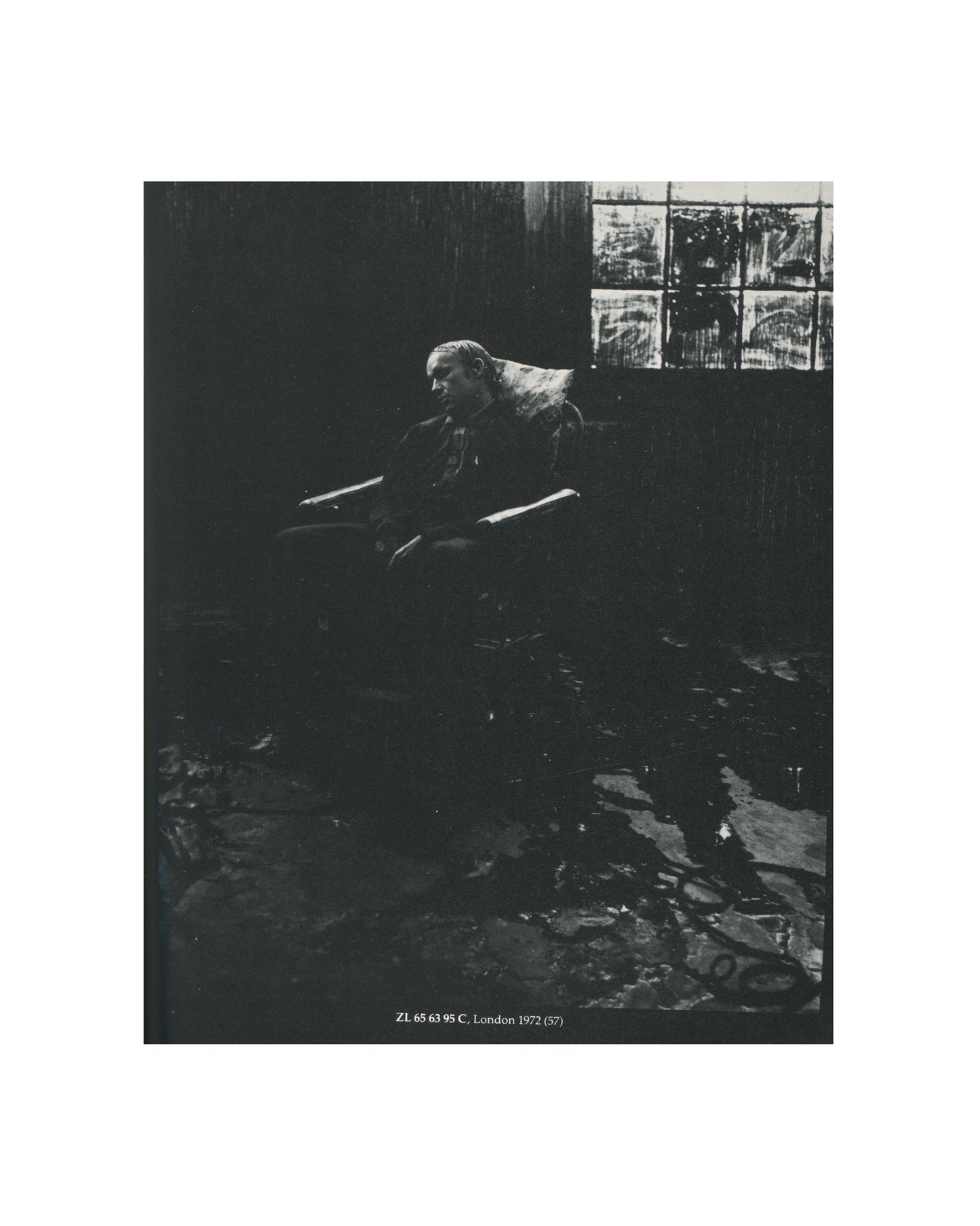 `Stuart Brisley — ICA, London, 1981 — interior plate. Black and white photograph documenting performance ZL 65 63 95 C, London, 1972. Brisley seated in a darkened room, debris and liquid covering the floor, paint-marked window behind. Caption: "ZL 65 63 95 C, London 1972 (57)."`