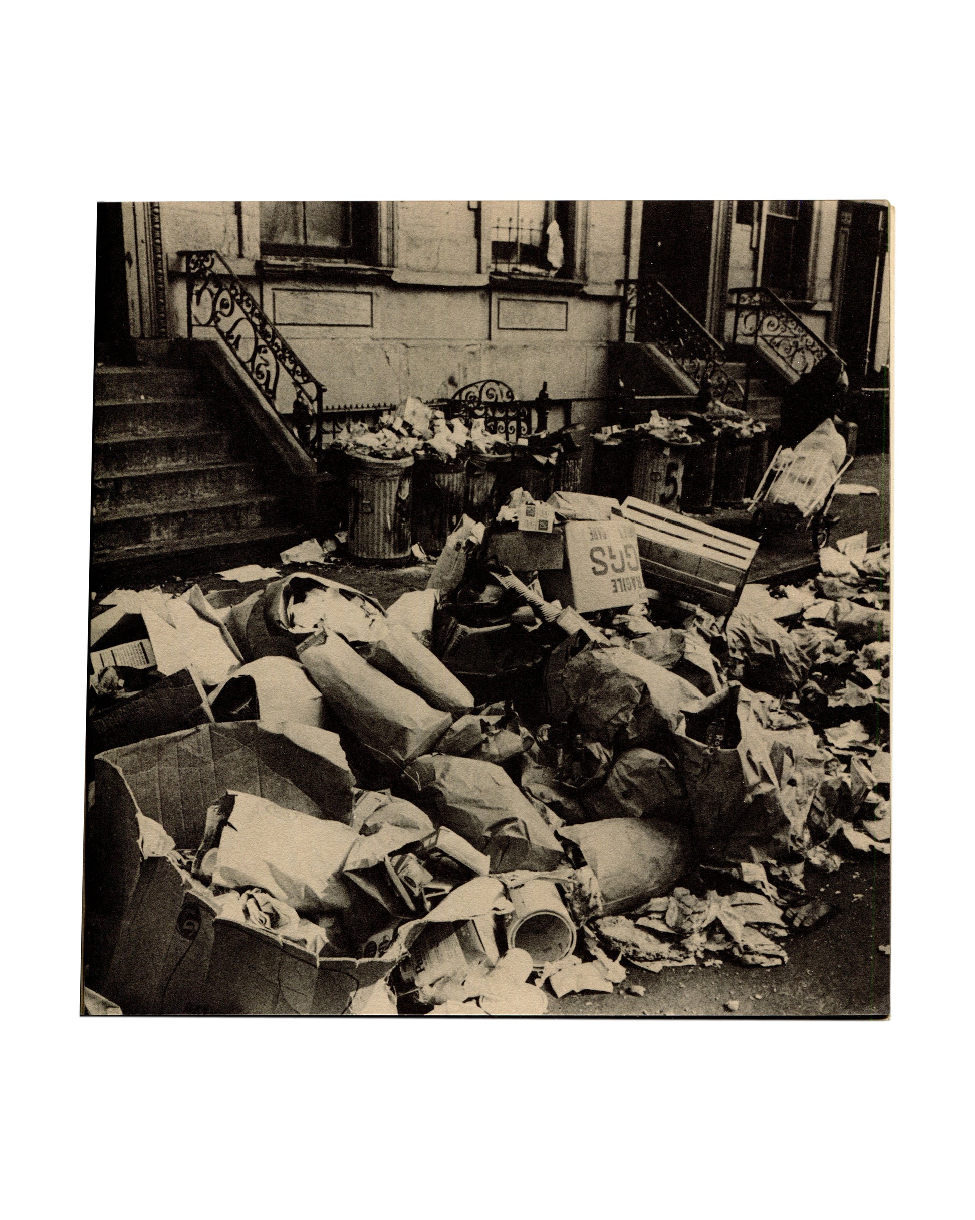 Interior spread. Left page showing a black-and-white documentary photograph of overflowing refuse bins and scattered rubbish on a New York street in front of a brownstone building with iron railings.