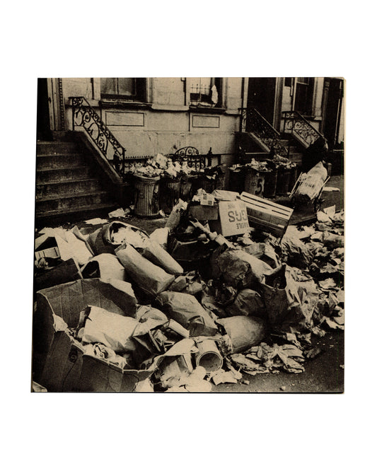 Interior spread. Left page showing a black-and-white documentary photograph of overflowing refuse bins and scattered rubbish on a New York street in front of a brownstone building with iron railings.