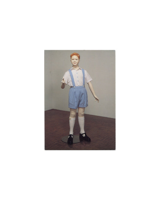 Postcard recto, Charles Ray, Boy, Whitney Museum of American Art, New York, 1997. Offset colour reproduction. Full-length view of sculpture — life-size figure of a boy with short red hair, pale complexion; white short-sleeve shirt with blue buttons, blue shorts with braces/suspenders, white knee socks, black Mary Jane shoes; standing on small black metal base against neutral grey gallery wall and dark wood floor. Painted fiberglass, steel, and fabric. Light surface marks, good vintage condition.

