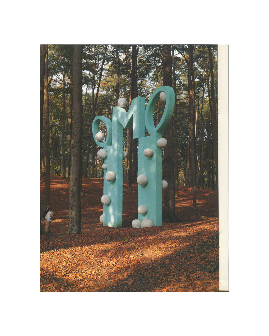 Jiří Georg Dokoupil, Exhibition Catalogue, 1987 — interior plate. Teal sculptural form with looping script-like structure and white spheres installed among pine trees on a leaf-covered forest floor.