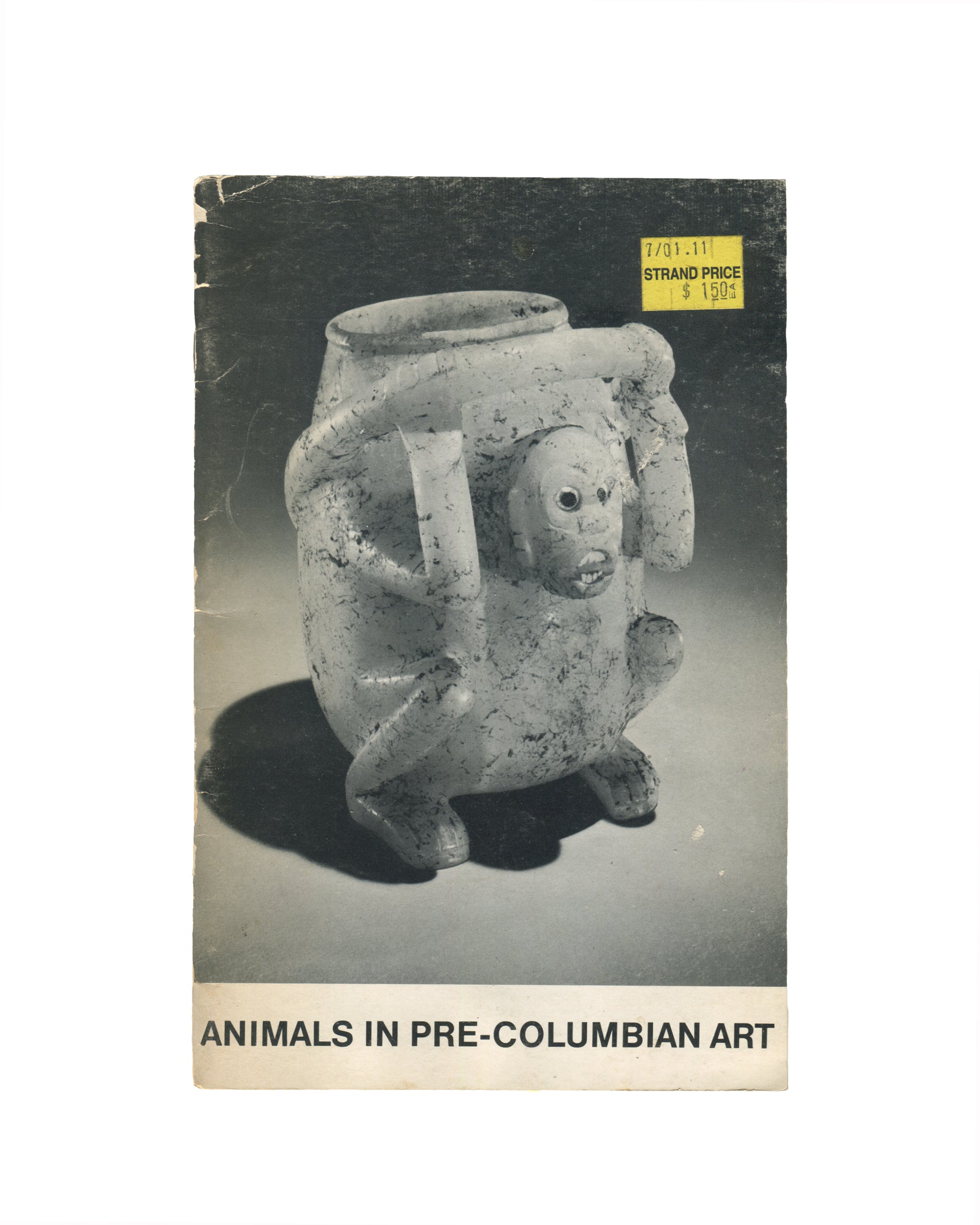 `Animals in Pre-Columbian Art — André Emmerich Gallery, New York — exhibition catalogue front cover. Black and white photograph of a Pre-Columbian ceramic effigy vessel: a squat, four-legged jar with a zoomorphic face — wide-set eyes, open mouth with teeth, and stubby limbs — on a grey ground. Yellow Strand Bookstore price sticker upper right ($15.00). Title in black sans-serif at foot: "ANIMALS IN PRE-COLUMBIAN ART".`