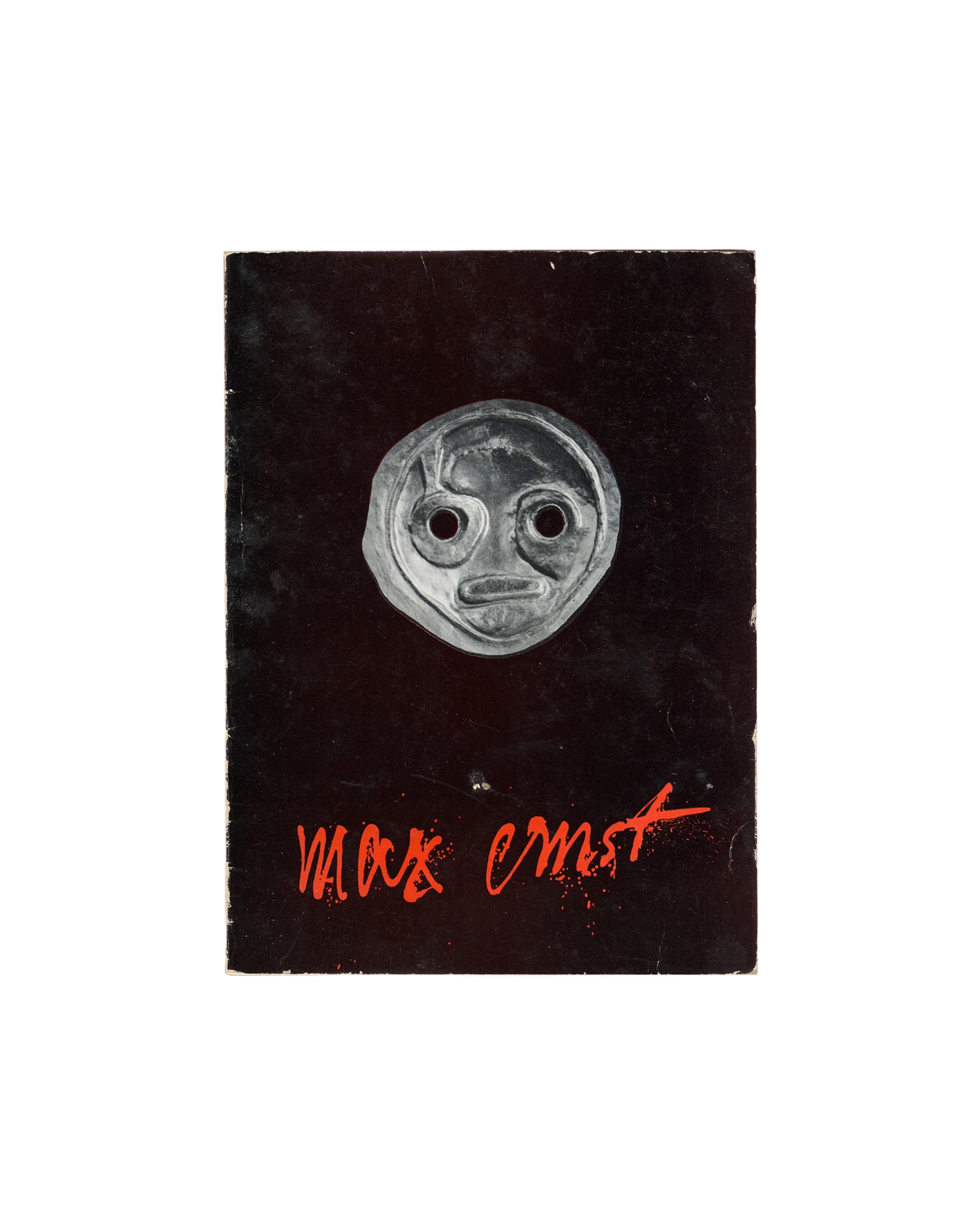 Front cover Max Ernst, 1959. Black cover: silver mask sculpture centre, red handwritten 'max ernst' lower right. Rubbing and corner wear. 