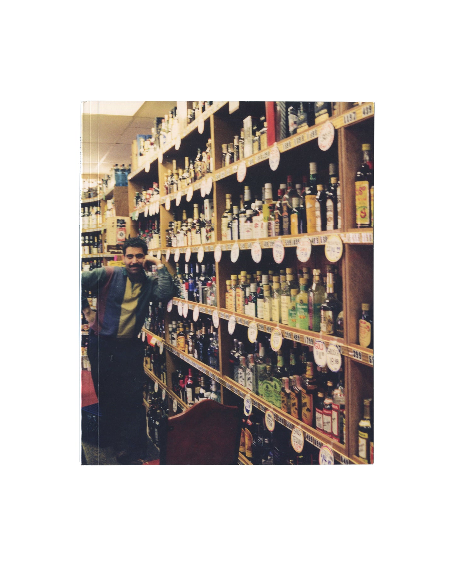 Reverse of 2015 Mark Grotjahn K&H Liquors artist book, Karma, New York. Back cover showing a figure standing in a liquor store aisle with floor-to-ceiling shelves of bottles, photographed in warm ambient light.