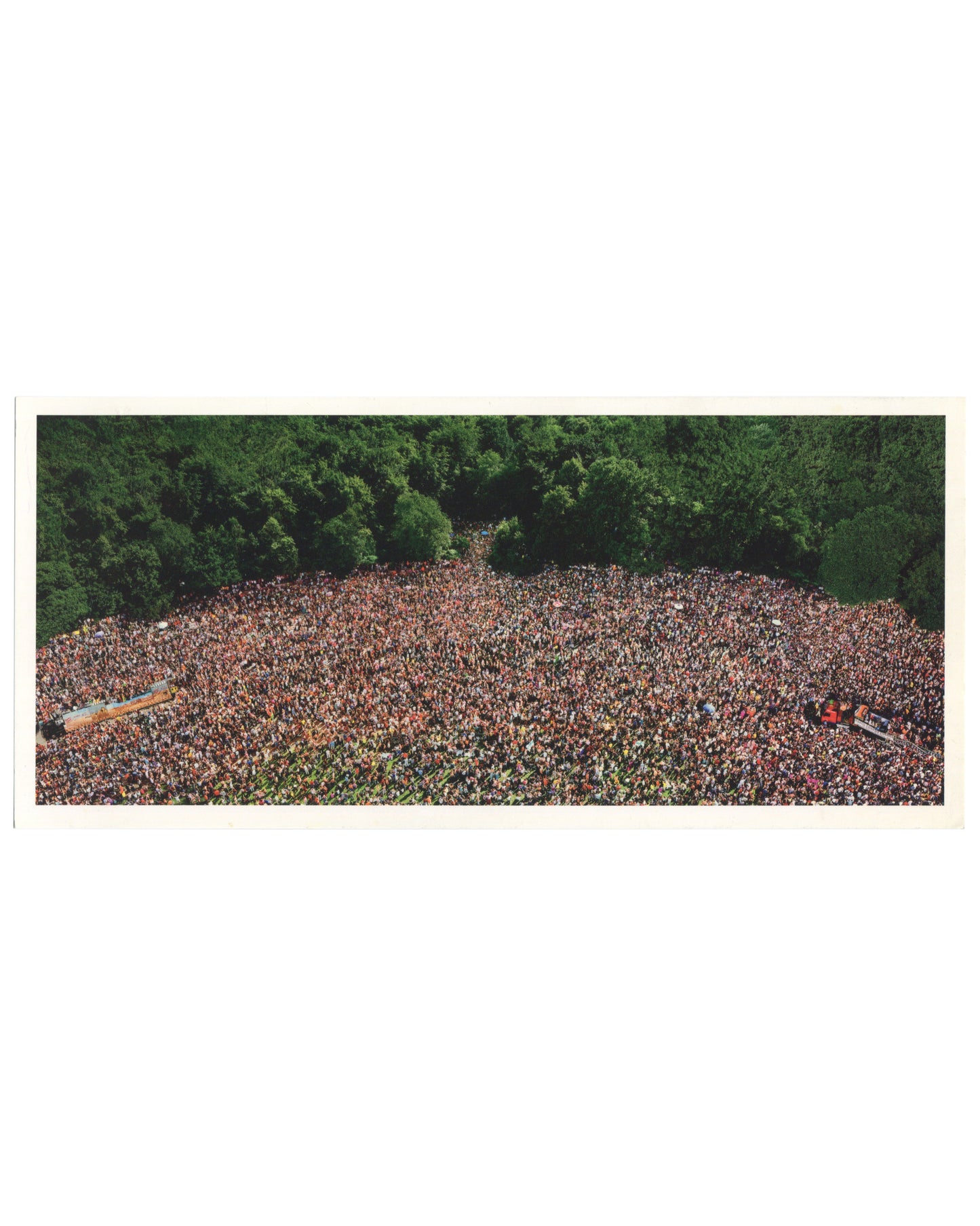 Andreas Gursky, Love Parade, 2001, artist postcard recto. Matthew Marks Gallery, New York, 2001. Colour reproduction of a large-format C-print: aerial view of an enormous crowd filling a clearing in a dense green forest, photographed from directly above. The mass of people — hundreds of thousands — forms an irregular oval shape, their individual figures indistinguishable at this scale, creating a dense texture of skin tones, clothing, and colour. Two long vehicles or floats are visible at the left and lower