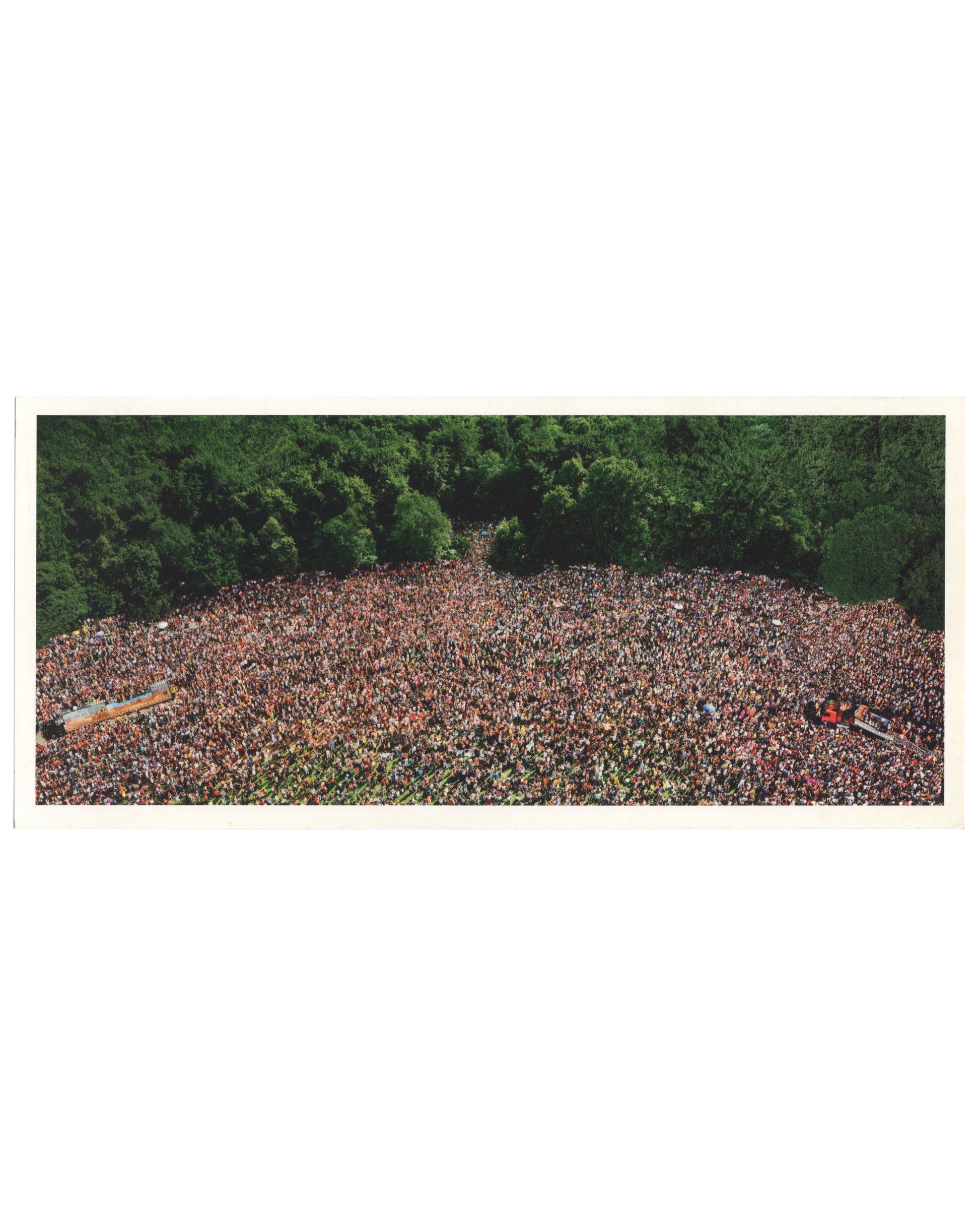 Andreas Gursky, Love Parade, 2001, artist postcard recto. Matthew Marks Gallery, New York, 2001. Colour reproduction of a large-format C-print: aerial view of an enormous crowd filling a clearing in a dense green forest, photographed from directly above. The mass of people — hundreds of thousands — forms an irregular oval shape, their individual figures indistinguishable at this scale, creating a dense texture of skin tones, clothing, and colour. Two long vehicles or floats are visible at the left and lower