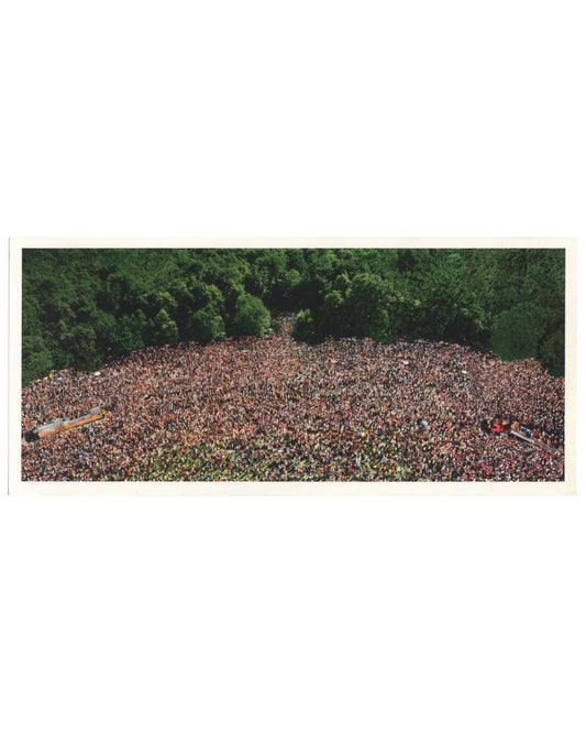 Andreas Gursky, Love Parade, 2001, artist postcard recto. Matthew Marks Gallery, New York, 2001. Colour reproduction of a large-format C-print: aerial view of an enormous crowd filling a clearing in a dense green forest, photographed from directly above. The mass of people — hundreds of thousands — forms an irregular oval shape, their individual figures indistinguishable at this scale, creating a dense texture of skin tones, clothing, and colour. Two long vehicles or floats are visible at the left and lower