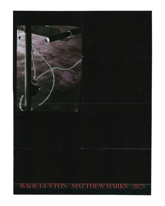 Original exhibition poster, Wade Guyton, Matthew Marks Gallery, New York, September 14 – October 28, 2023. Offset lithograph, 46 × 61 cm. Folded as issued. Black ground. Upper left: large colour photograph inset — close-up of a metal studio rack or table leg with a coiled black-and-white striped cable or hose looping across a dark floor surface. Remainder of poster: solid black. Lower margin: red serif text 'WADE GUYTON  MATTHEW MARKS  2023'. Horizontal fold lines visible across full poster surface; light h