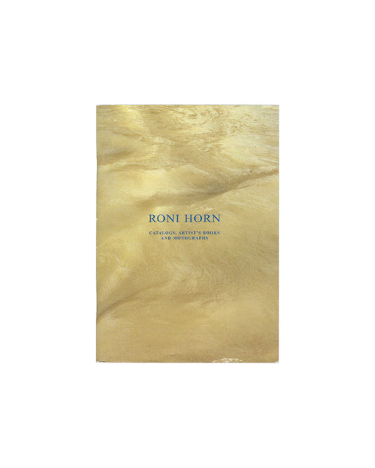 Front cover Roni Horn, Catalogs, Artist's Books and Monographs, Edizioni Periferia / a+mbookstore Edizioni, 2004. Front cover: metallic gold reflective wrappers with rippled, cloud-like surface texture in warm gold and pale yellow tones; "RONI HORN" in small spaced blue serif capitals centre; "CATALOGS, ARTIST'S BOOKS / AND MONOGRAPHS" in smaller spaced blue serif type below. Softcover, staple-bound, 10.5 × 15 cm. Rubbing, surface marks and light scratching visible across wrappers.