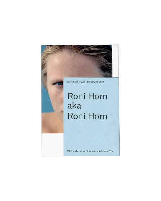  Back cover — colour portrait with overwrap Roni Horn aka Roni Horn, Whitney Museum of American Art, New York, 2009. Exhibition guide back cover: pale blue printed overwrap overlaid on self-wrapper; overwrap carries "November 6, 2009–January 24, 2010" in small dark grey sans-serif type upper left; "Roni Horn / aka / Roni Horn" in large dark grey sans-serif type centre left; "Whitney Museum of American Art, New York" in small dark grey sans-serif type lower left; behind overwrap, colour close-up photograph o