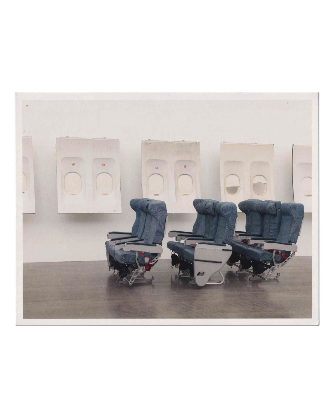 Isa Genzken, Window, exhibition invitation front. Hauser & Wirth, London, 2020. Colour photograph of installation view: three rows of blue economy-class aircraft seats on a dark wood floor, with a row of white airplane window panels mounted on the gallery wall behind. Untitled (detail), 2018. Photo: Todd White Art Photography.