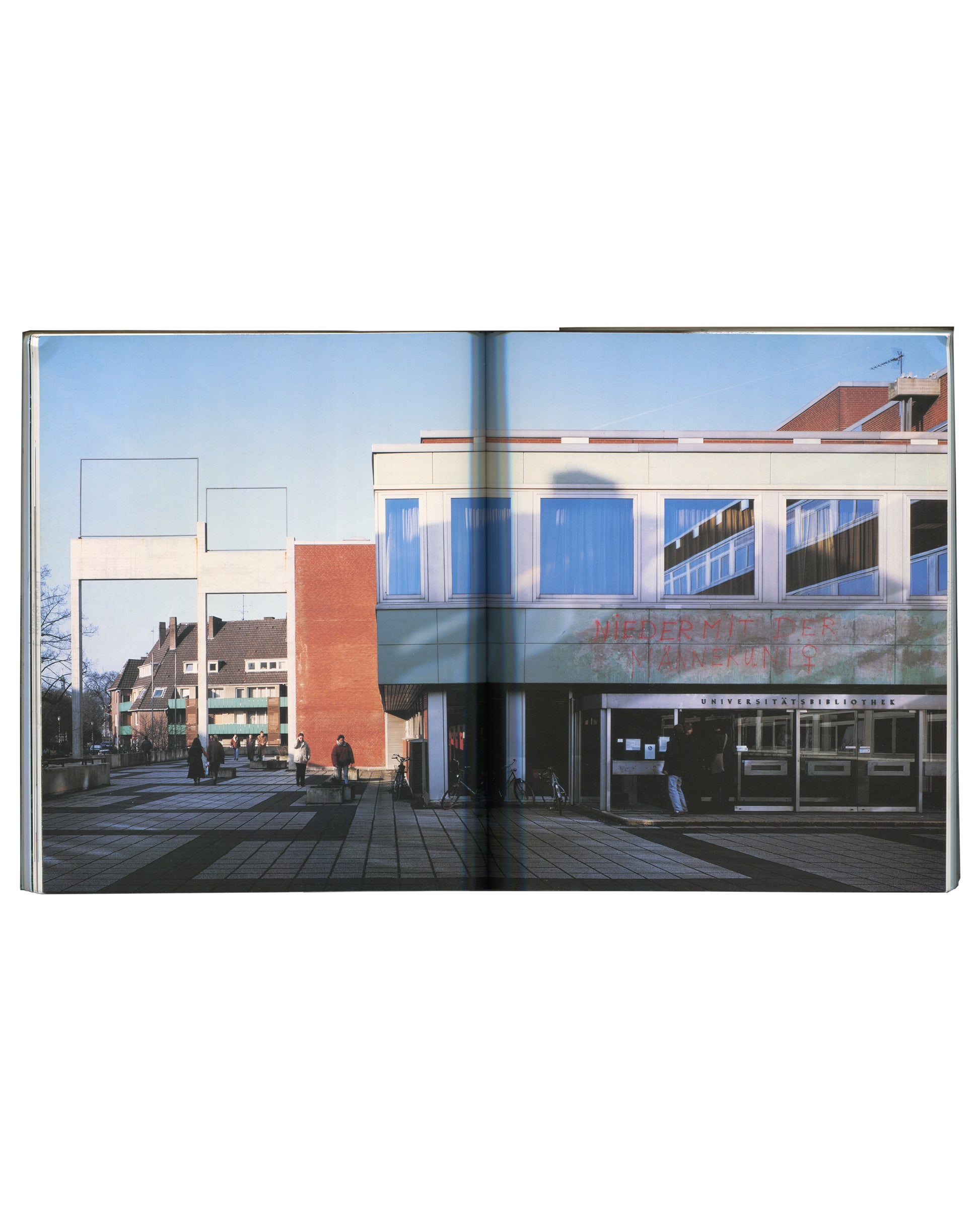 Full-bleed double-page photograph of a German university library building with Genzken's two white rectangular frame sculptures on poles in the plaza.