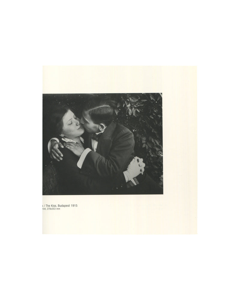 Early photograph The Kiss, Budapest (1915), depicting a formally dressed couple embracing beneath foliage.

