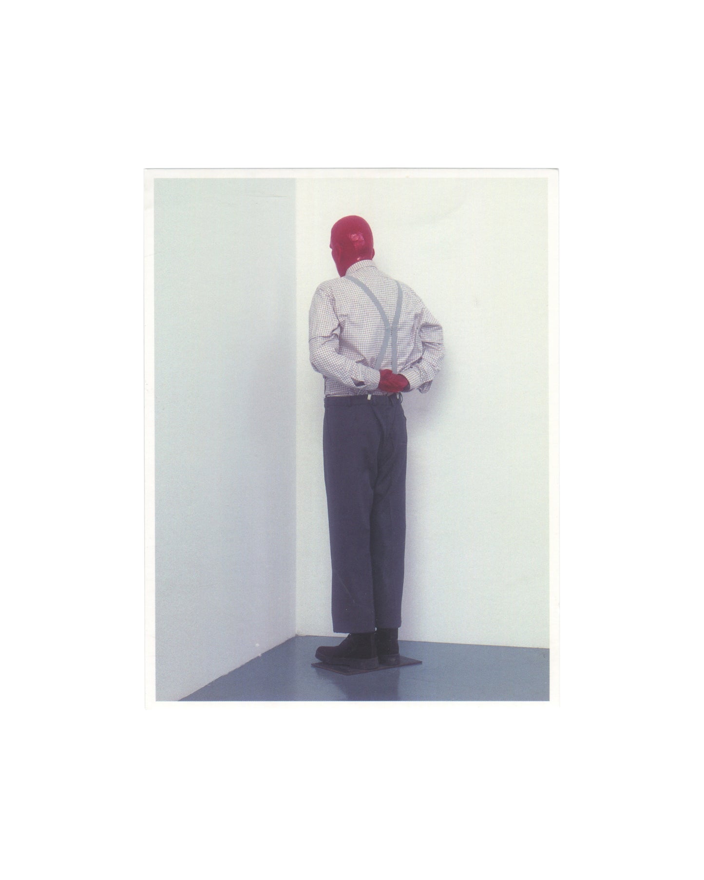 Original 2006 Edition 5 artist postcard reproducing Martin Kippenberger's sculpture Martin, ab in die Ecke und schäm dich, 1989, showing a life-size resin figure of a man in a checked shirt, braces, grey trousers, and black shoes, standing with his back to the viewer, face pressed into the corner of two white gallery walls, arms clasped behind his back, the figure photographed in a clean white gallery space with a grey floor.