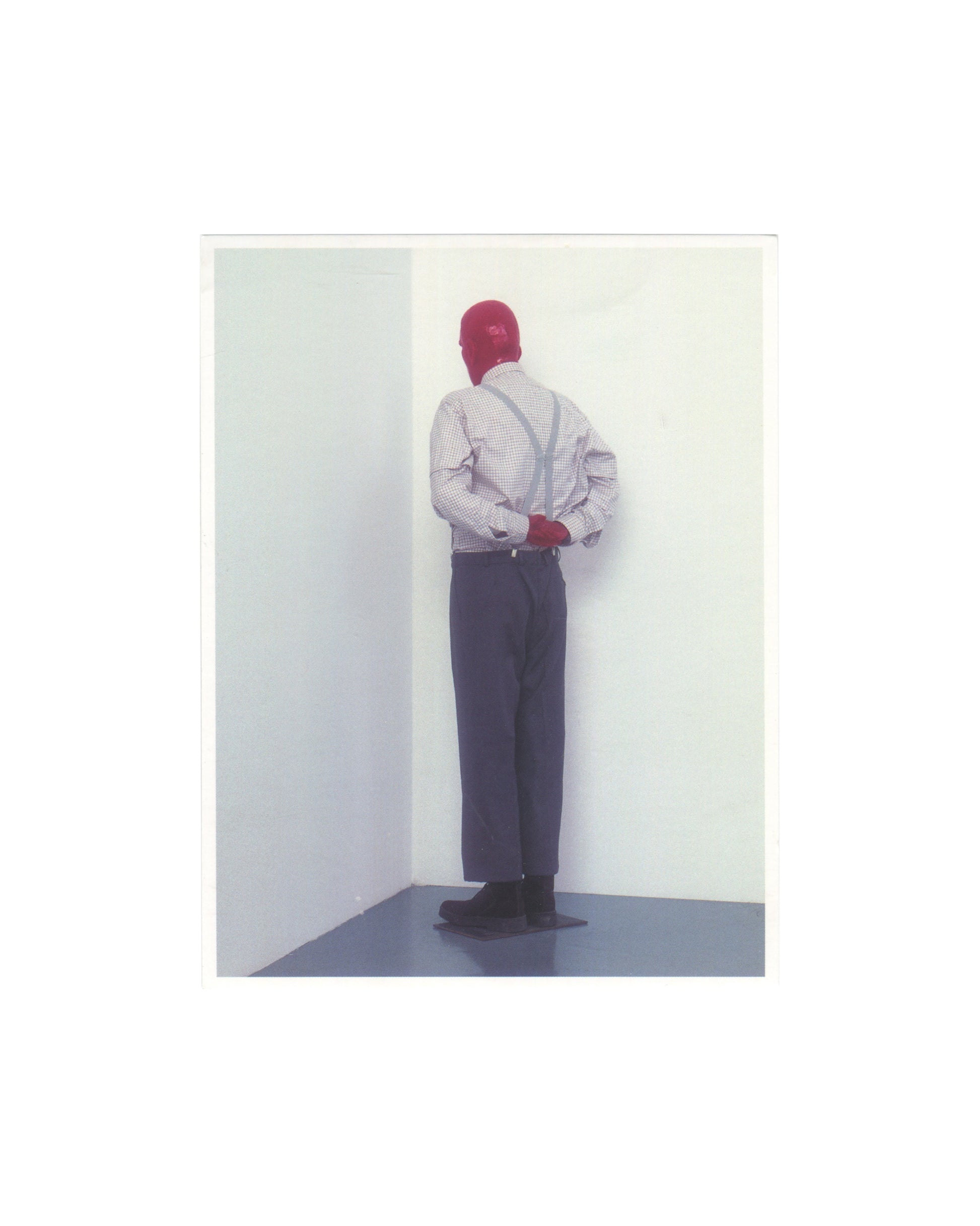 Original 2006 Edition 5 artist postcard reproducing Martin Kippenberger's sculpture Martin, ab in die Ecke und schäm dich, 1989, showing a life-size resin figure of a man in a checked shirt, braces, grey trousers, and black shoes, standing with his back to the viewer, face pressed into the corner of two white gallery walls, arms clasped behind his back, the figure photographed in a clean white gallery space with a grey floor.