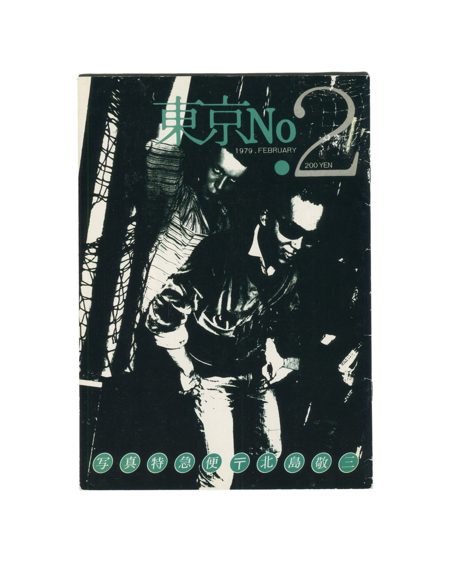 `Keizō Kitajima — 東京 No. 2 (Tokyo No. 2), Photo Express Tokyo, February 1979. Front cover. High-contrast black and white photograph of two figures in close proximity, faces partially obscured, one in a leather jacket, set against a dark ground with diagonal structural elements. Title in teal kanji and Latin type upper centre: 東京 No 2. Date and price: 1979. FEBRUARY · 200 YEN. Green circular stamps along foot reading: 写 真 特 急 便 〒 北 島 敬 三 (Photo Express Mail, Kitajima Keizō).`