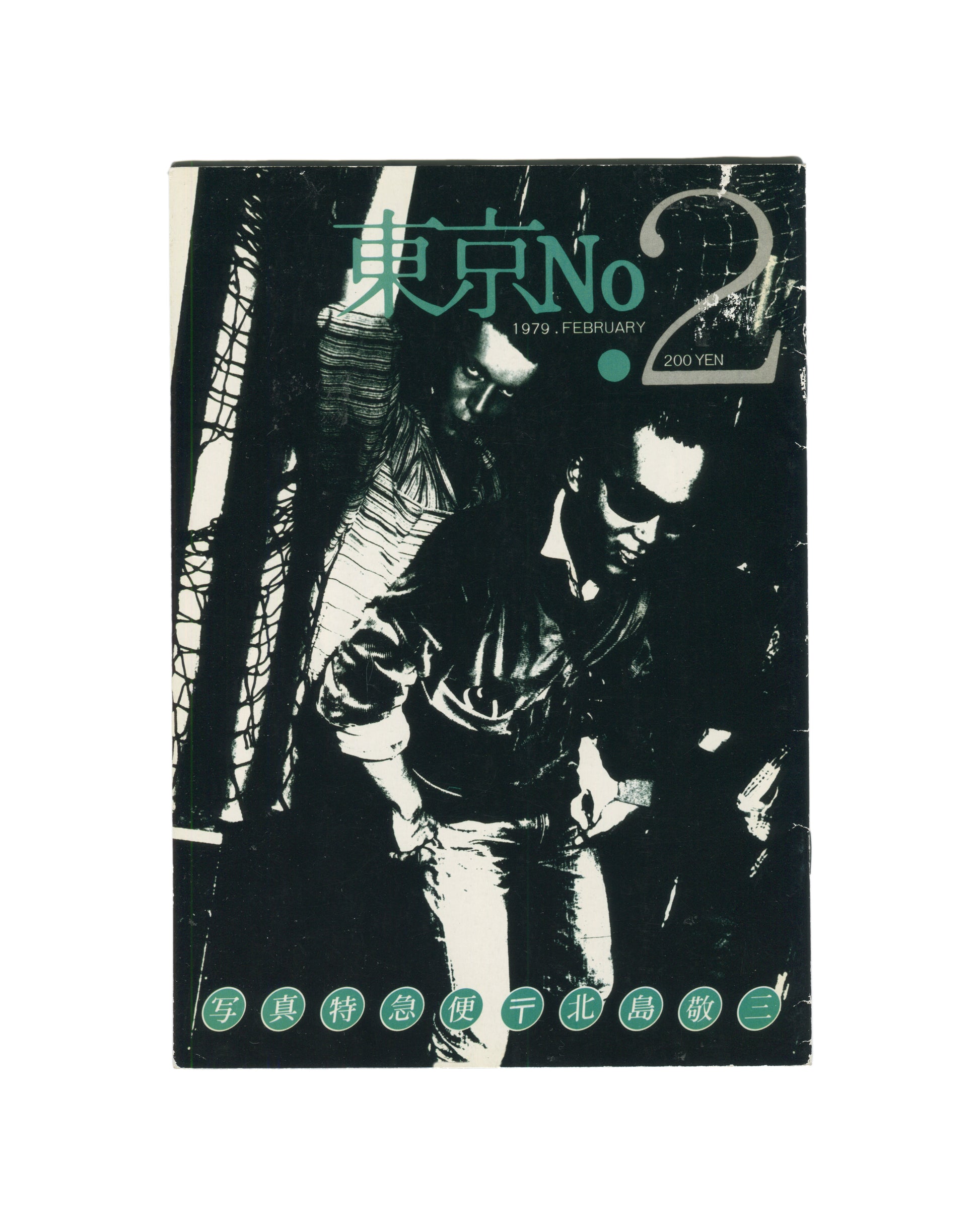 `Keizō Kitajima — 東京 No. 2 (Tokyo No. 2), Photo Express Tokyo, February 1979. Front cover. High-contrast black and white photograph of two figures in close proximity, faces partially obscured, one in a leather jacket, set against a dark ground with diagonal structural elements. Title in teal kanji and Latin type upper centre: 東京 No 2. Date and price: 1979. FEBRUARY · 200 YEN. Green circular stamps along foot reading: 写 真 特 急 便 〒 北 島 敬 三 (Photo Express Mail, Kitajima Keizō).`