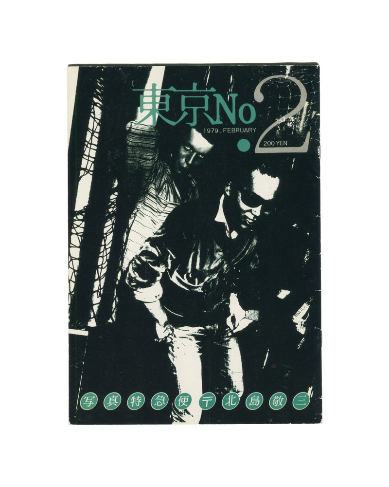 `Keizō Kitajima — 東京 No. 2 (Tokyo No. 2), Photo Express Tokyo, February 1979. Front cover. High-contrast black and white photograph of two figures in close proximity, faces partially obscured, one in a leather jacket, set against a dark ground with diagonal structural elements. Title in teal kanji and Latin type upper centre: 東京 No 2. Date and price: 1979. FEBRUARY · 200 YEN. Green circular stamps along foot reading: 写 真 特 急 便 〒 北 島 敬 三 (Photo Express Mail, Kitajima Keizō).`