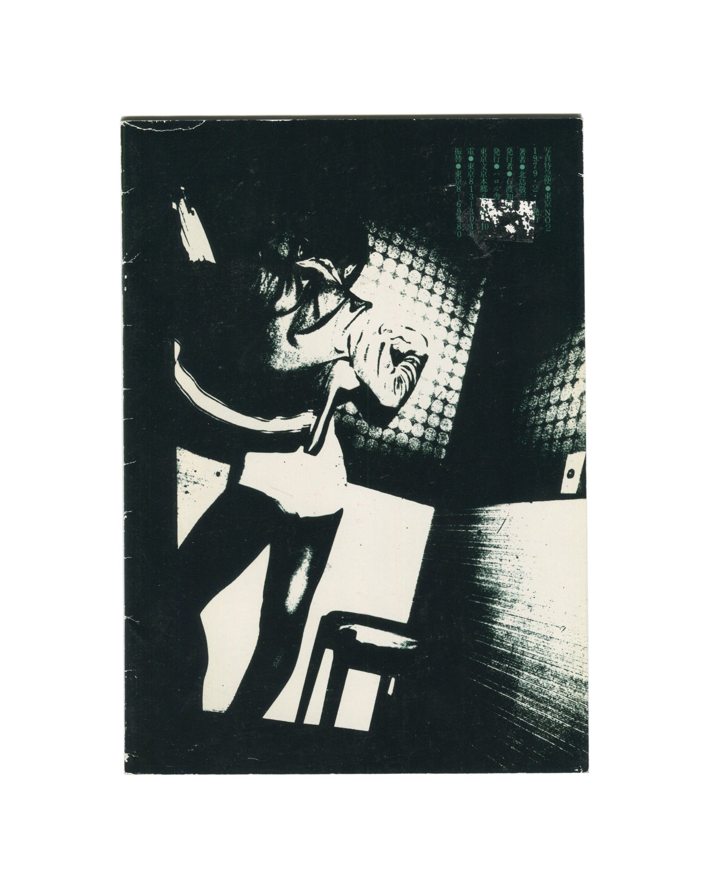 `Keizō Kitajima — Photo Express Tokyo No. 2, February 1979 — back cover. High-contrast black and white photograph of a figure leaning back over a chair, mouth open, arm raised, face caught in flash light against a patterned background. Small teal text block and postage stamp upper right. Staple binding visible at left spine. Heavy wear and creasing to covers.`