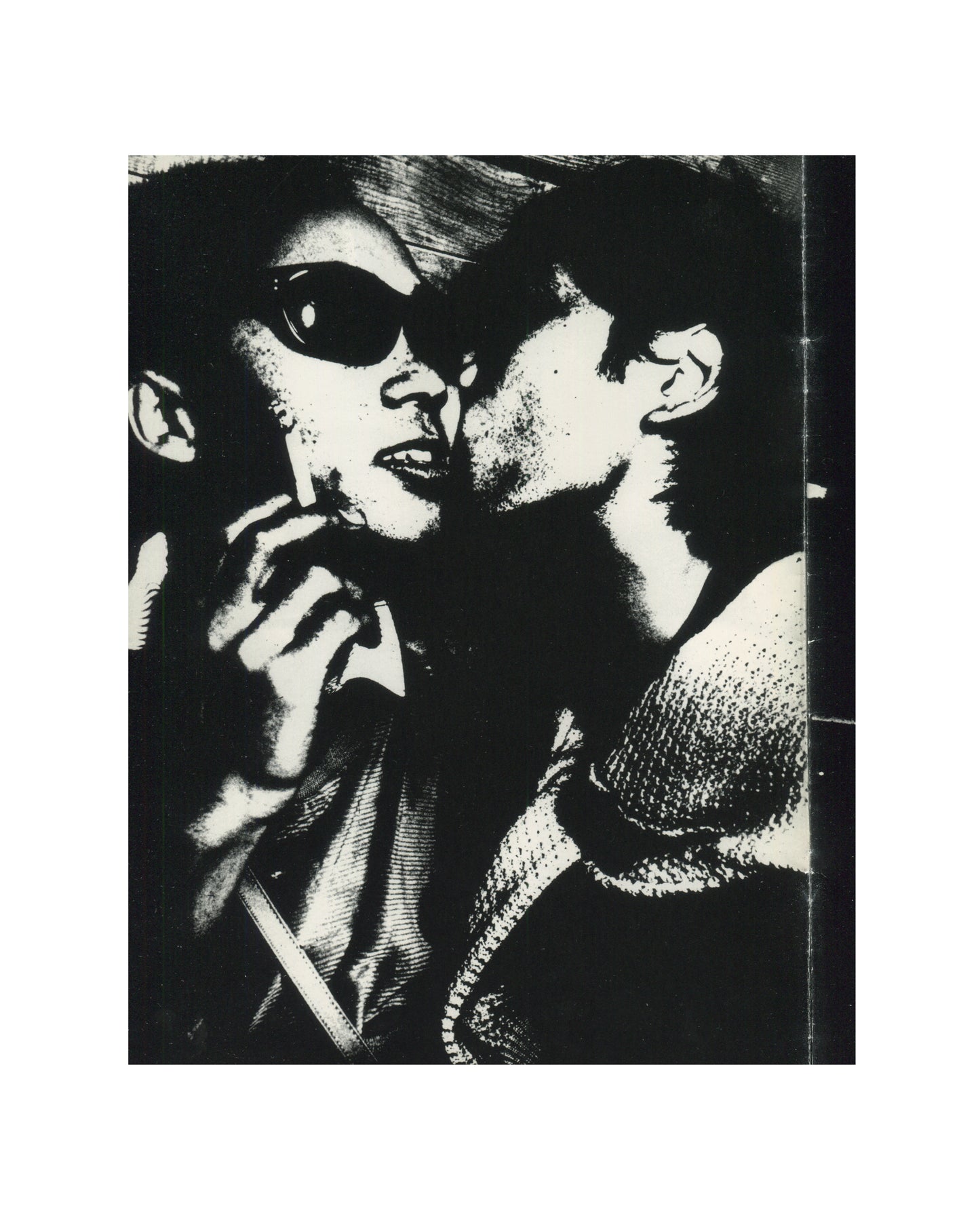 `Keizō Kitajima — Photo Express Tokyo No. 2, February 1979 — interior plate. High-contrast black and white photograph of two figures in extreme close-up: a woman wearing large dark sunglasses holding a cigarette, mouth slightly open, face turned toward a second figure whose lips are close to her cheek. Grain pushed to near-abstraction. Tokyo nightlife, 1979.`