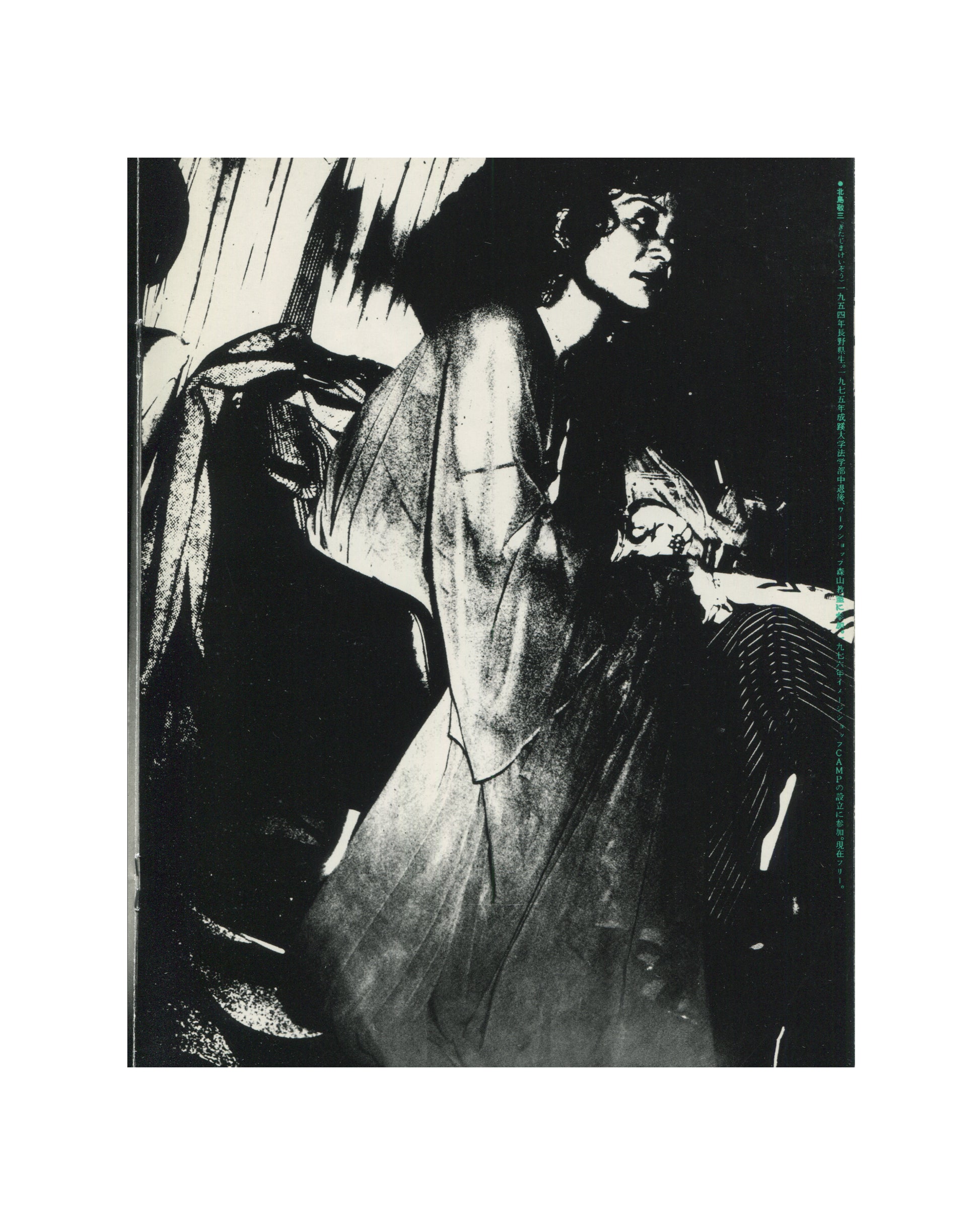 `Keizō Kitajima — Photo Express Tokyo No. 2, February 1979 — interior plate. High-contrast black and white photograph of a woman standing in a darkened interior, face turned upward in profile, wearing a sheer or satin robe-like garment that catches the light. Vertical streaks of flash illumination against deep black. Japanese text column in teal ink along right margin. Tokyo nightlife, 1979.`