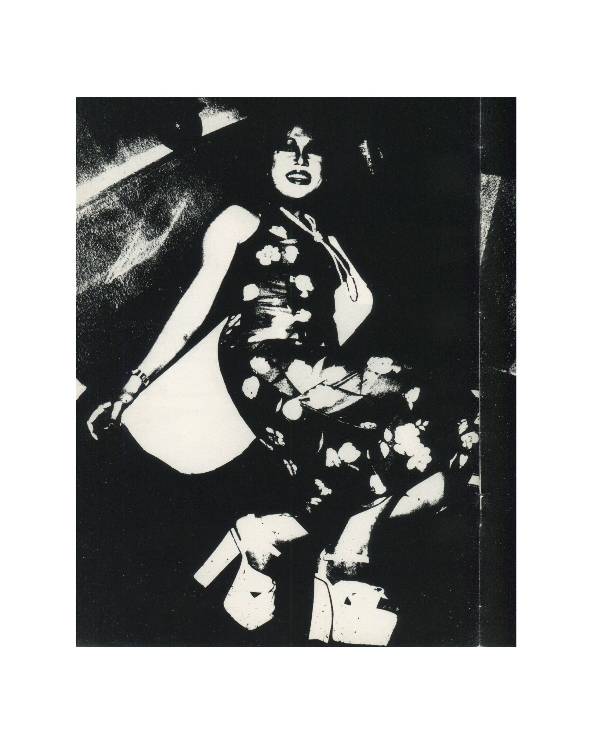 `Keizō Kitajima — Photo Express Tokyo No. 2, February 1979 — interior plate. High-contrast black and white photograph of a woman seated at low angle, wearing a floral-patterned qipao dress, platform shoes, and a wide-brimmed hat. Face tilted upward, smiling, body angled toward camera. Flash-bleached highlights against deep black ground. Tokyo nightlife, 1979.`
