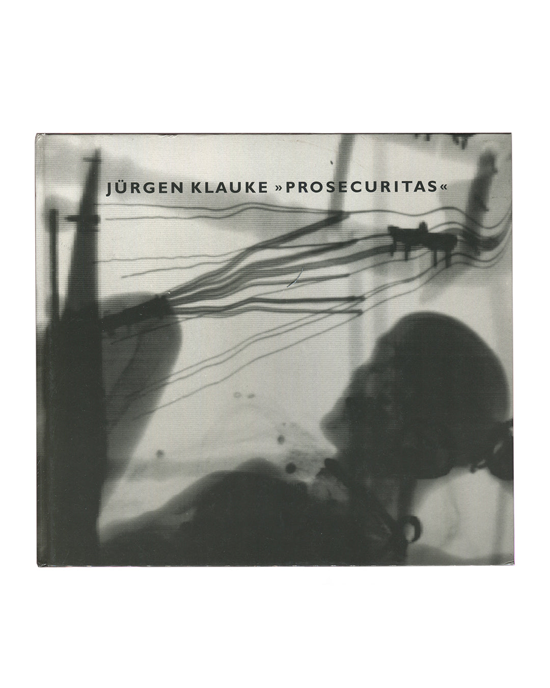 Original 1994 Jürgen Klauke Prosecuritas exhibition catalogue. Front cover showing a black-and-white scanned or photocopied image: two small dog silhouettes walk across a pale ground trailing long curved lines, while large dark shadowy forms — a vertical pole left and a crouching figure lower right — dominate the foreground. Title 'JÜRGEN KLAUKE »PROSECURITAS«' in small spaced sans-serif type upper centre. Square format, cloth-bound hardcover with clear plastic dust jacket.
