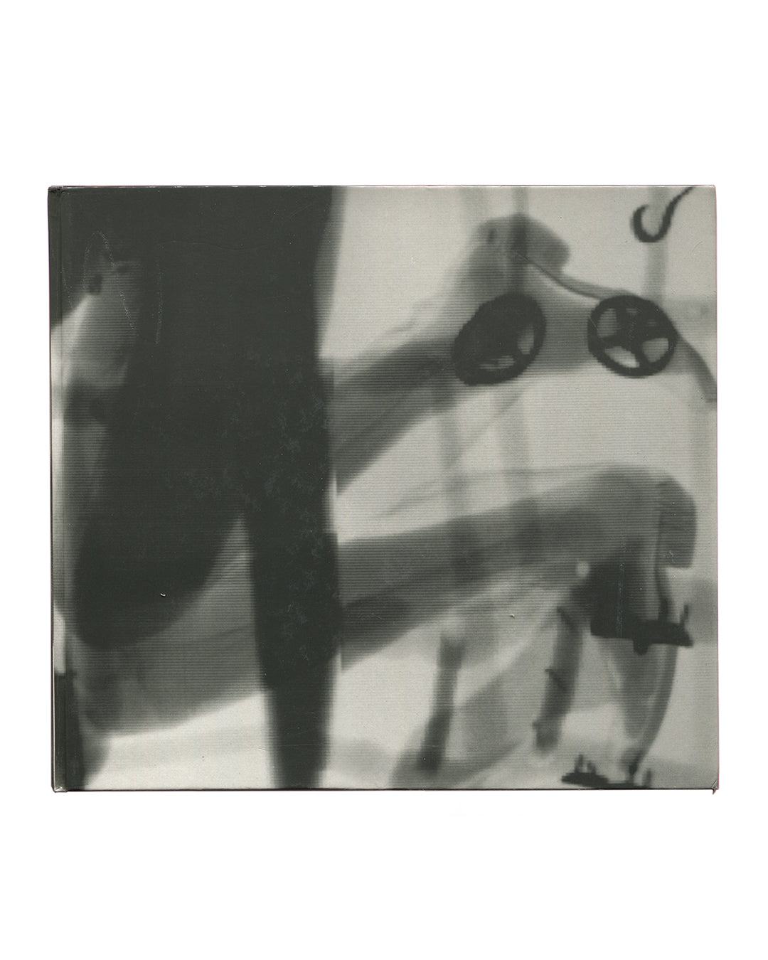 Reverse of 1994 Jürgen Klauke Prosecuritas exhibition catalogue. Back cover showing a black-and-white scanned image: a large dark vertical form occupies the left half, while the right half shows a blurred interior scene with a child's tricycle, a small seated figure, and a curved hook or handle upper right. No text. Square format, cloth-bound hardcover with clear plastic dust jacket.