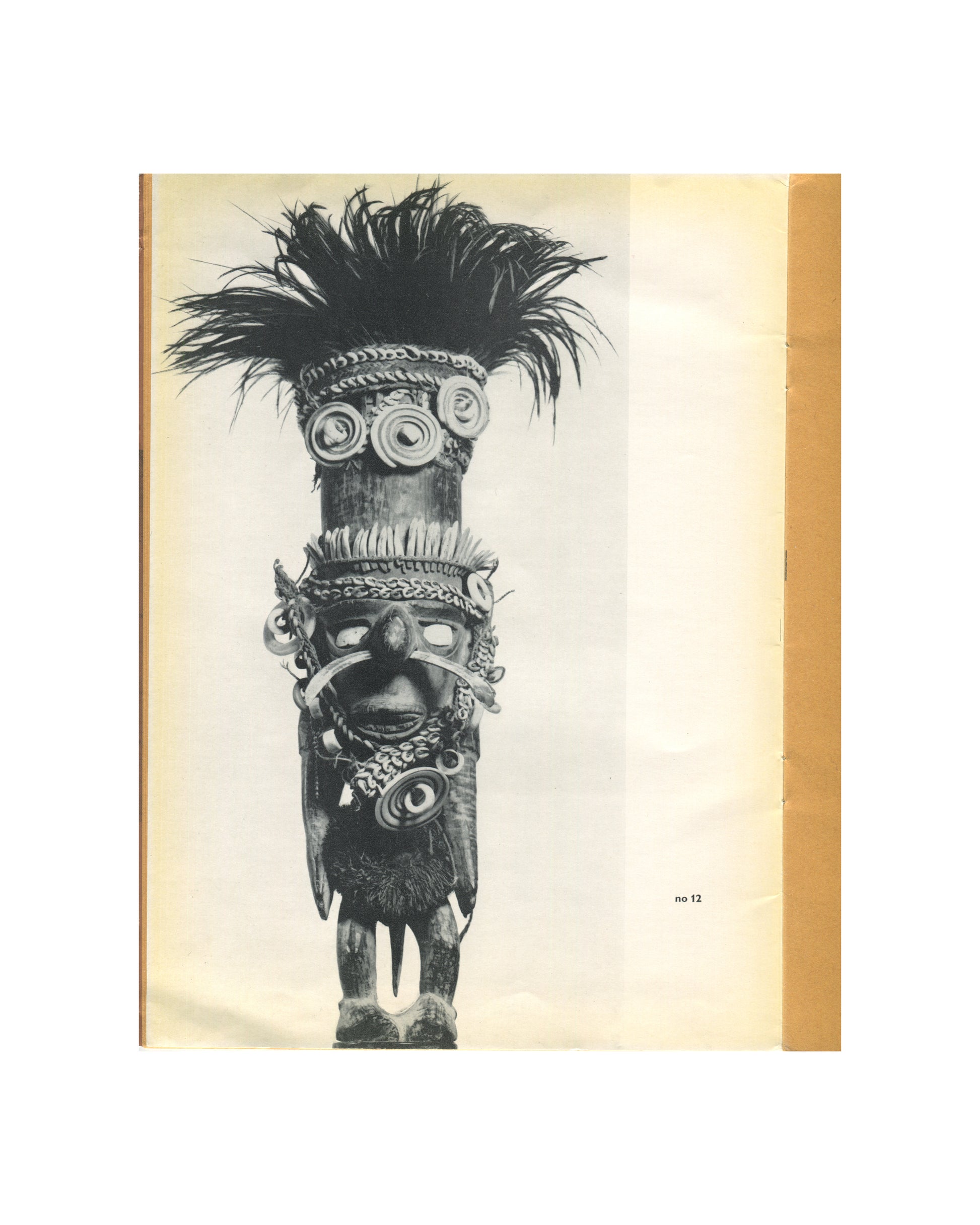 `Kunst uit Nieuw Guinea, 1963 — interior plate. Black and white photograph of catalogue no. 12: a tall ceremonial figure or skull pole, heavily adorned. Cylindrical carved wooden body surmounted by a face with shell and fibre ornaments, spiral shell discs at the brow, and a large crown of dark feathers radiating outward. Shell collar, pendant ornaments, and carved lower body with splayed feet. Photographed against pale ground.`