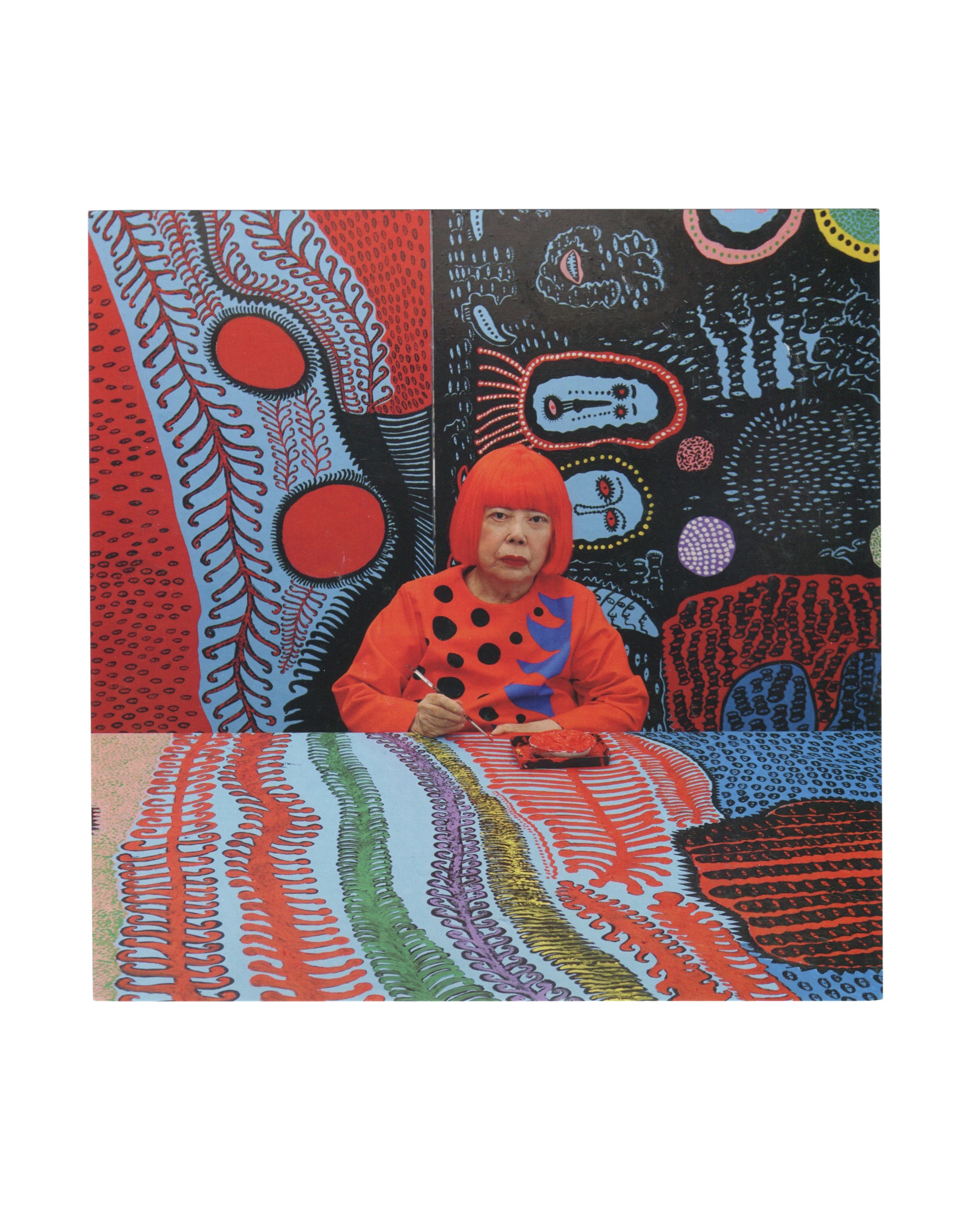 2017 Yayoi Kusama exhibition invitation card featuring a studio portrait of the artist seated at a table surrounded by vividly colored *My Eternal Soul* paintings. Kusama wears her signature bright red wig and an orange dress with black polka dots, visually blending into the dense field of reds, blues, dots, and biomorphic patterns surrounding her.
