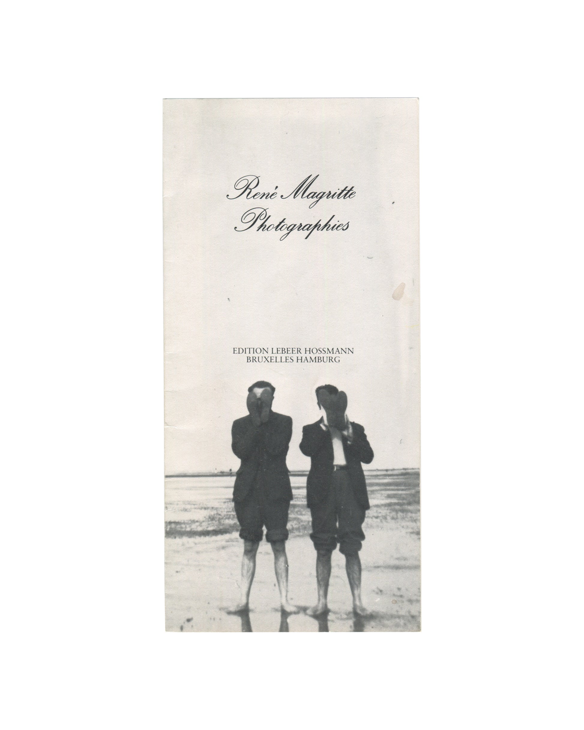1976 Edition Lebeer Hossmann publisher's brochure for René Magritte Photographies, front cover, showing René Magritte Photographies in italic script at the top, EDITION LEBEER HOSSMANN / BRUXELLES HAMBURG in small caps below, and a black-and-white photograph of two boys standing with their backs to the camera on a flat beach, their heads turned away, wearing dark jackets and shorts.