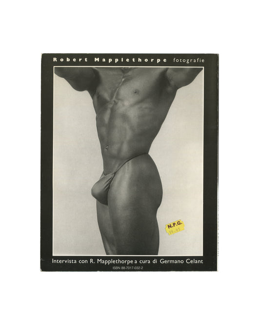 Robert Mapplethorpe — Fotografie, Idea Books Edizioni, Milan, 1983. Front cover. Black ground, title in spaced white capitals: 'Robert Mapplethorpe fotografie'. Centre: black-and-white photograph of a male torso in a white swimsuit, cropped at shoulders and thighs, high-contrast studio lighting. Lower text: 'Intervista con R. Mapplethorpe a cura di Germano Celant'. ISBN 88-7017-032-2. Original yellow N.P.G. price sticker lower right: 19.95. Photography monograph, Italian edition.