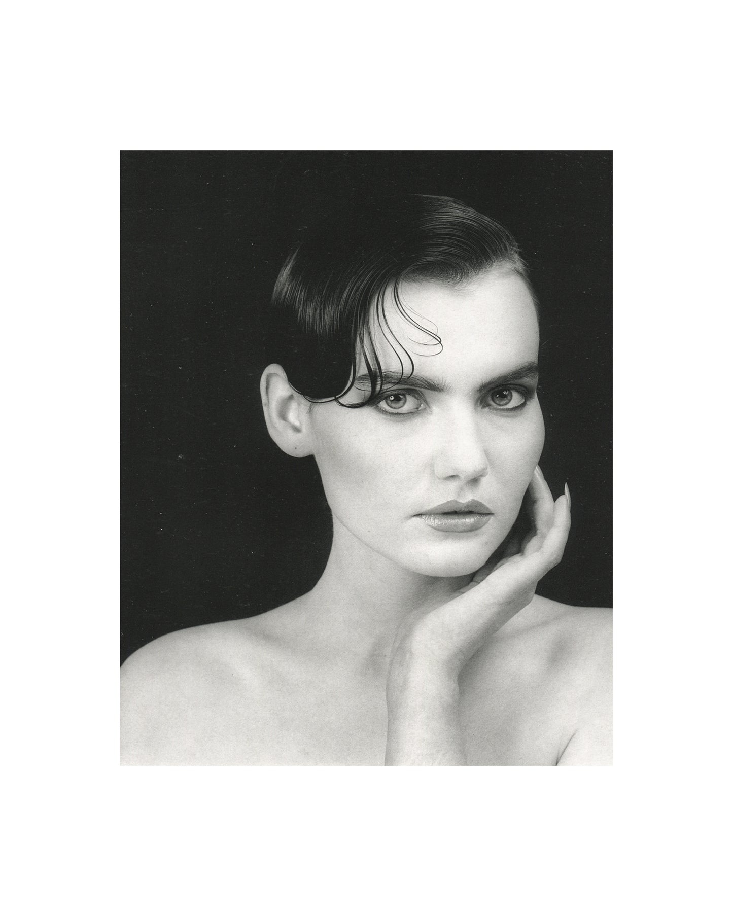 Robert Mapplethorpe — Fotografie, Idea Books Edizioni, Milan, 1983. Interior plate: black-and-white studio portrait. A woman with dark hair swept back and wet, bare-shouldered, hand raised to chin, direct gaze toward camera. Strong contrast against a black ground. Classical Mapplethorpe portraiture. Photography monograph, Germano Celant, The New Rare.