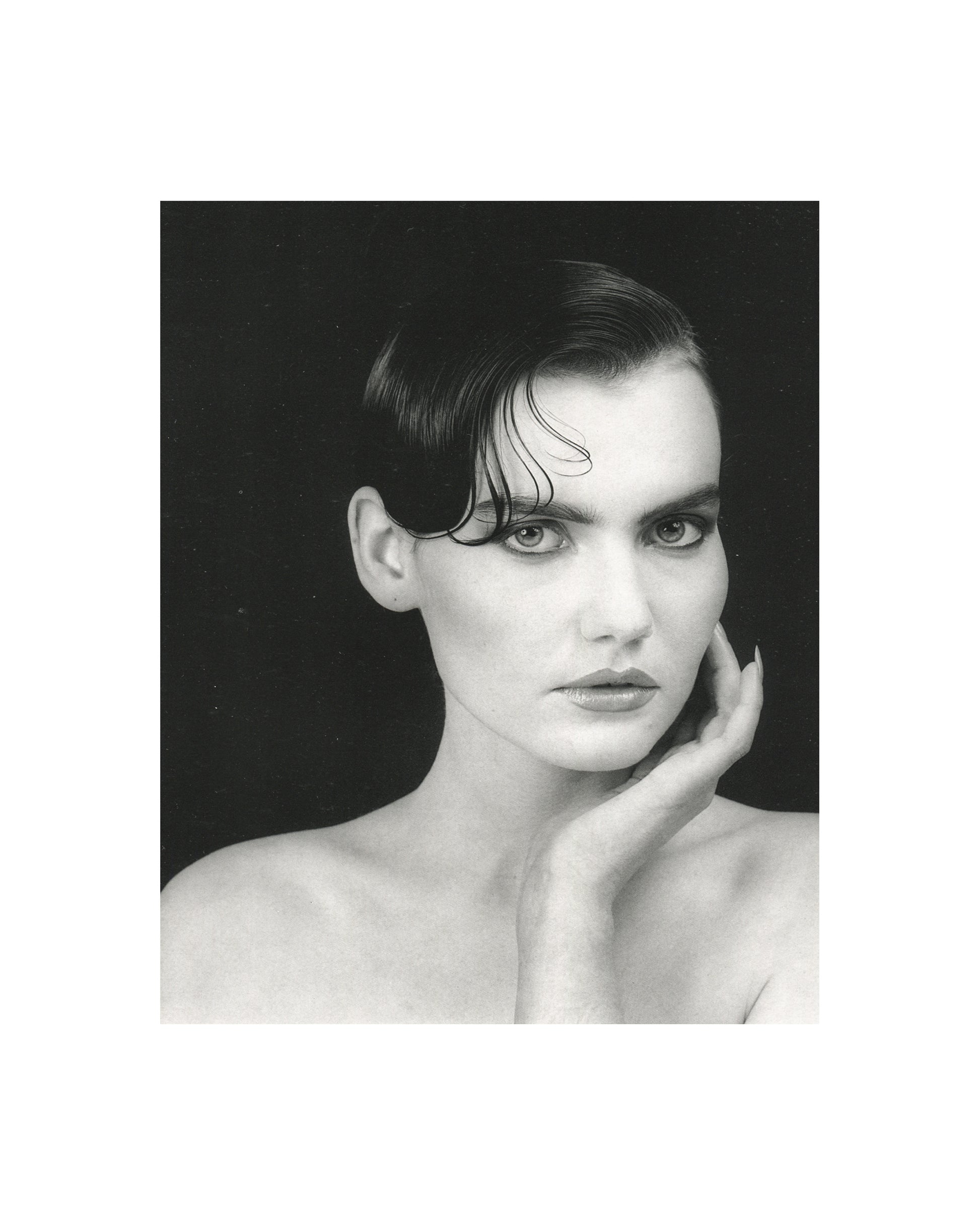 Robert Mapplethorpe — Fotografie, Idea Books Edizioni, Milan, 1983. Interior plate: black-and-white studio portrait. A woman with dark hair swept back and wet, bare-shouldered, hand raised to chin, direct gaze toward camera. Strong contrast against a black ground. Classical Mapplethorpe portraiture. Photography monograph, Germano Celant, The New Rare.