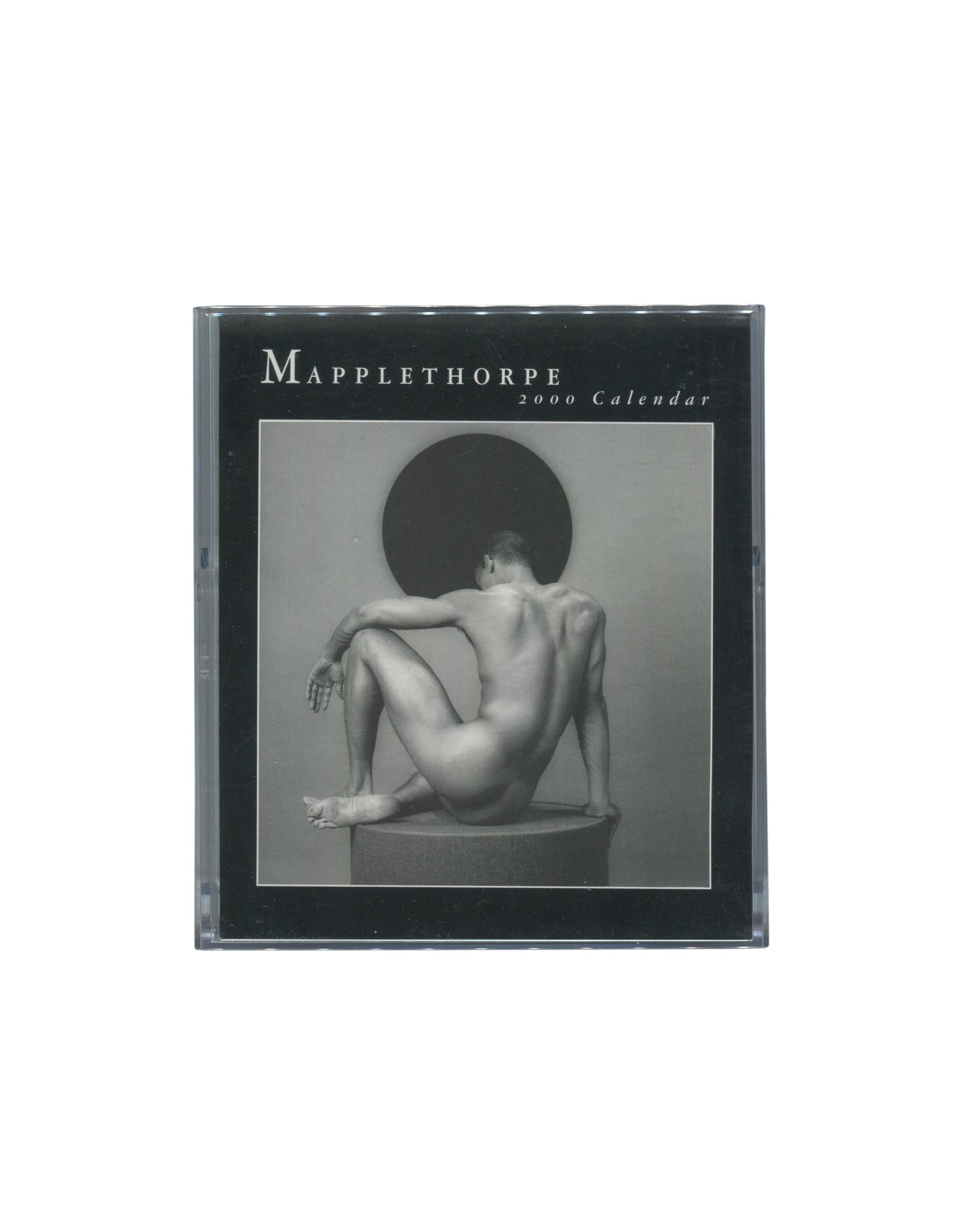 Cover insert of Robert Mapplethorpe, 2000 Calendar, CD case edition, teNeues, 1999, showing the calendar housed in a clear plastic CD jewel case, with a black printed insert reading MAPPLETHORPE / 2000 Calendar in white serif type at upper left, and a black-and-white photograph of a nude male figure seated on a plinth with his back to the camera, knees drawn up, against a circular dark disc.