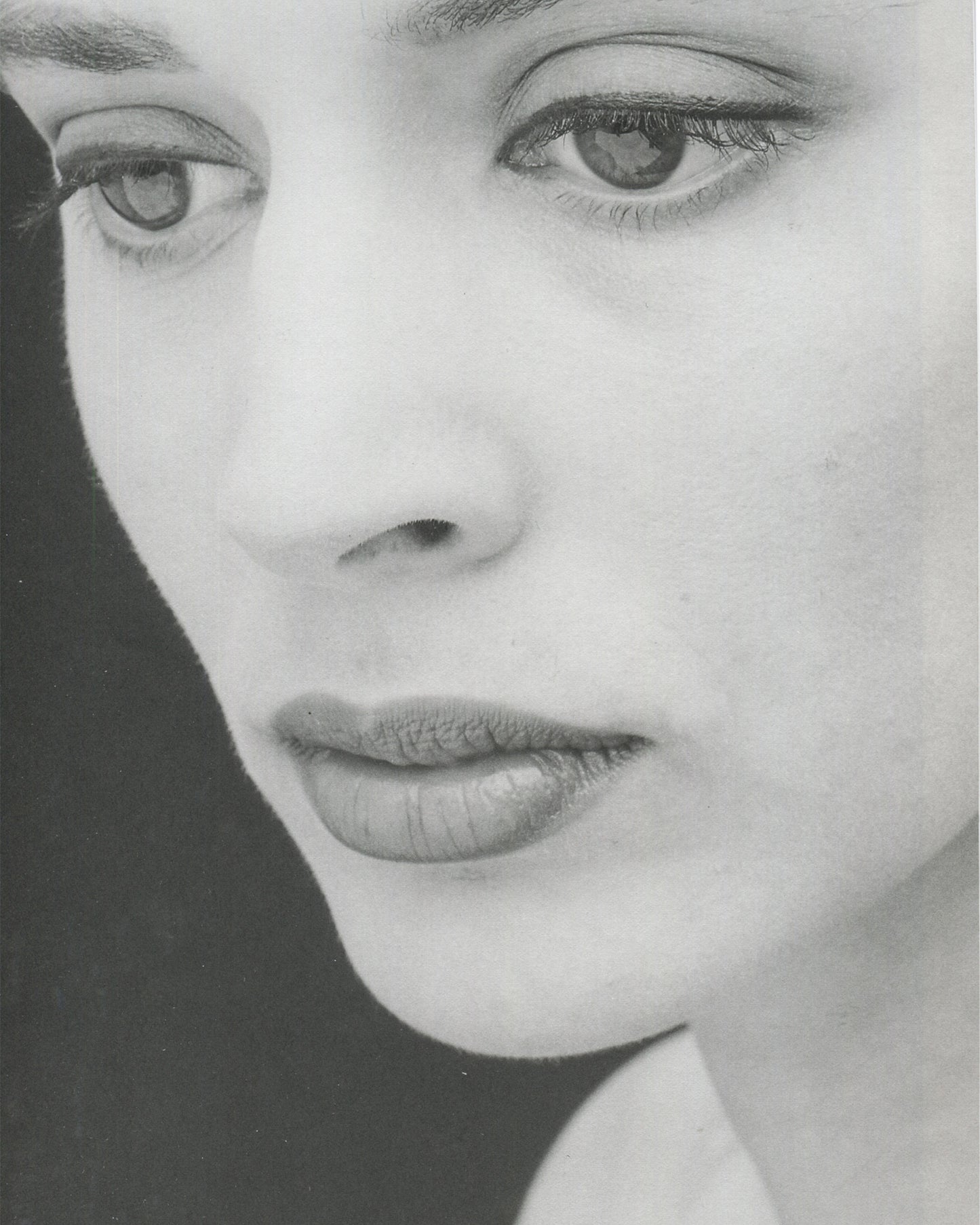 Interior page from Robert Mapplethorpe, Some Women, Bulfinch Press, 1992, showing a black-and-white extreme close-up of a woman's face cropped from the brow to the chin, the eyes gazing directly at the camera with a calm, neutral expression, the face lit to emphasise skin texture and the geometry of the features against a dark background.